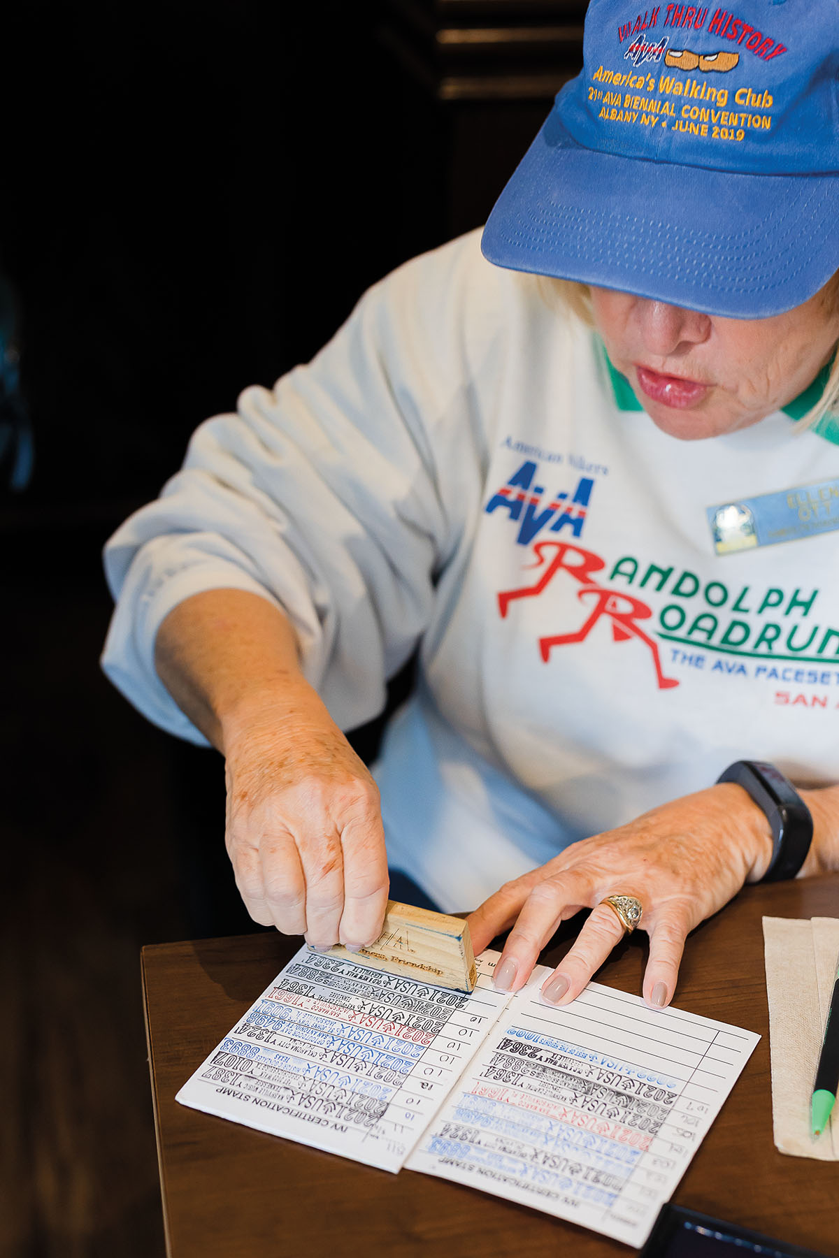 A woman in a blue hat and white sweatshirt writes information into a small cardstock log book