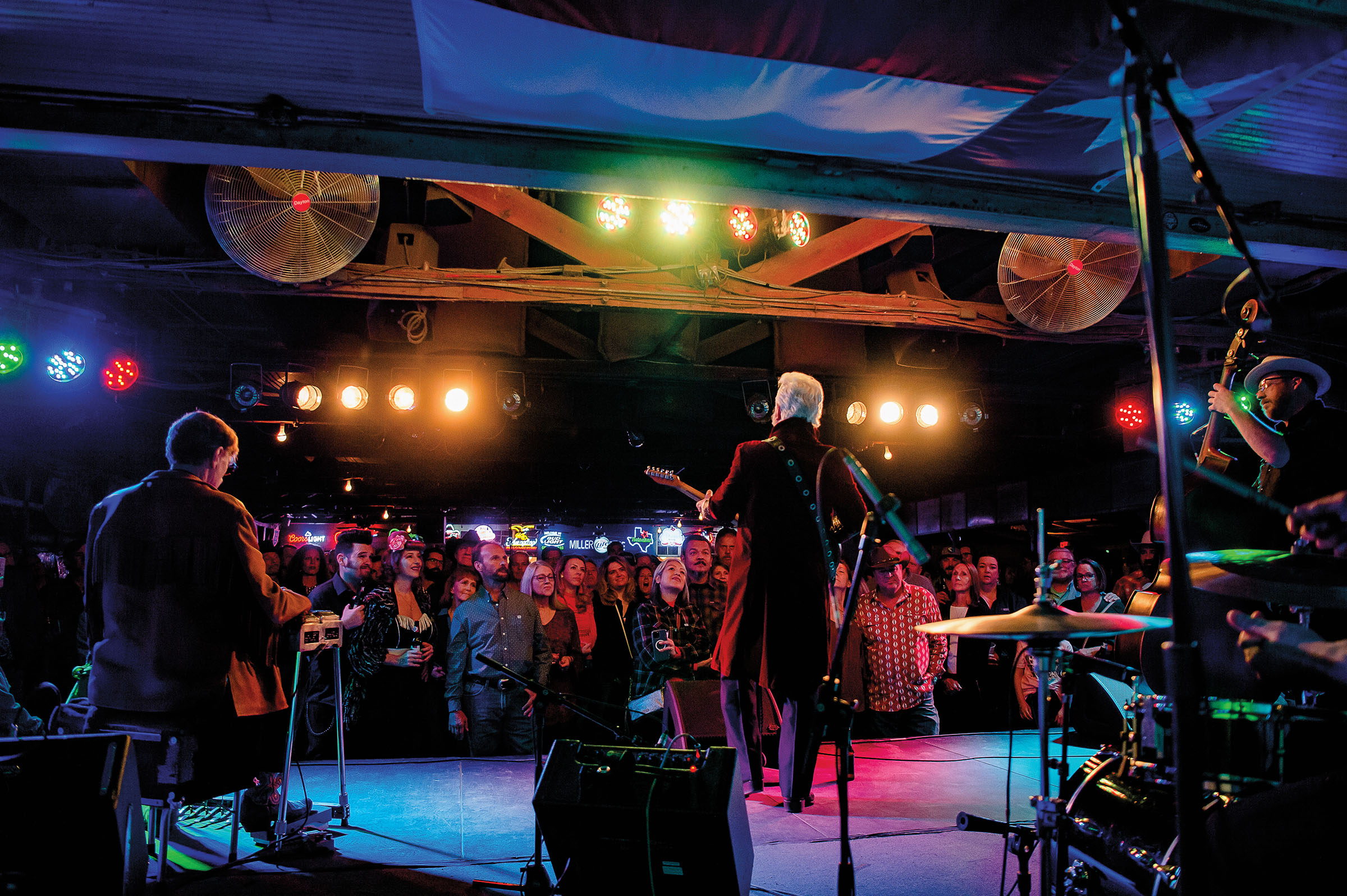 A picture of a man playing guitar under bright green, red and blue lights in front of a crowd of people