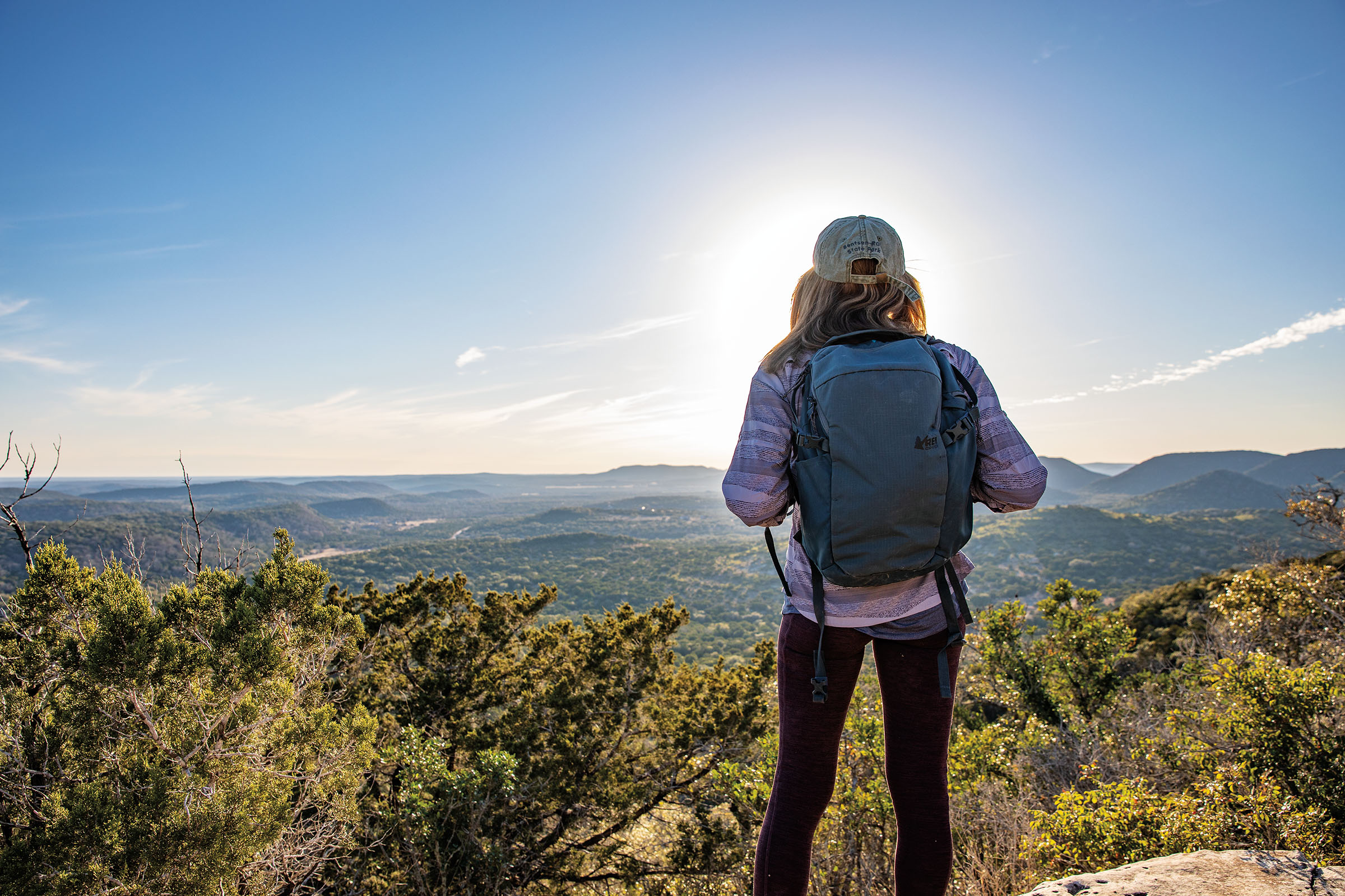 A picture of a person wearing a backpack standing on top of a tall hill overlooking a valley in sunshine