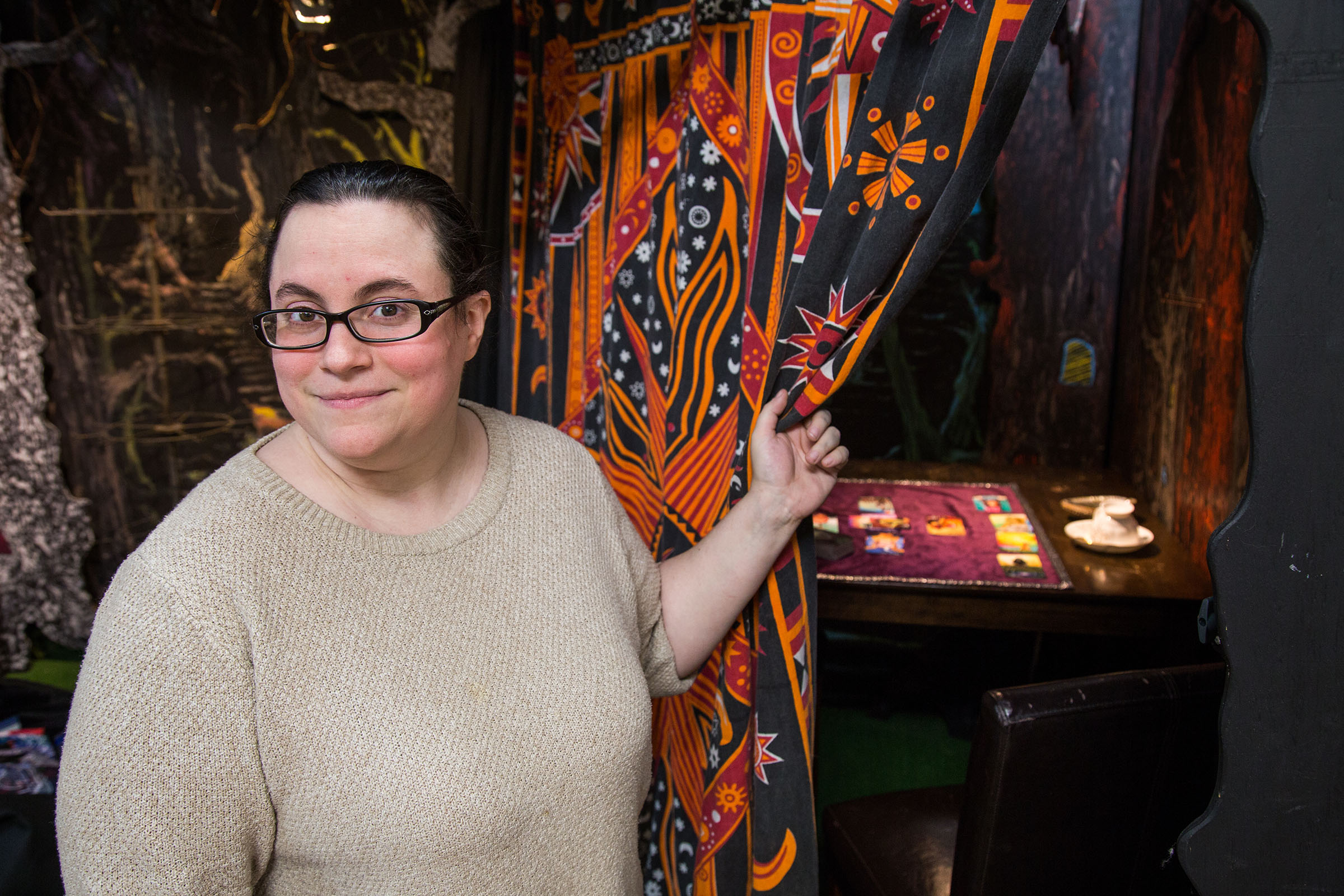 A picture of a woman standing in front of a brightly colored curtain pulled back to reveal a small room