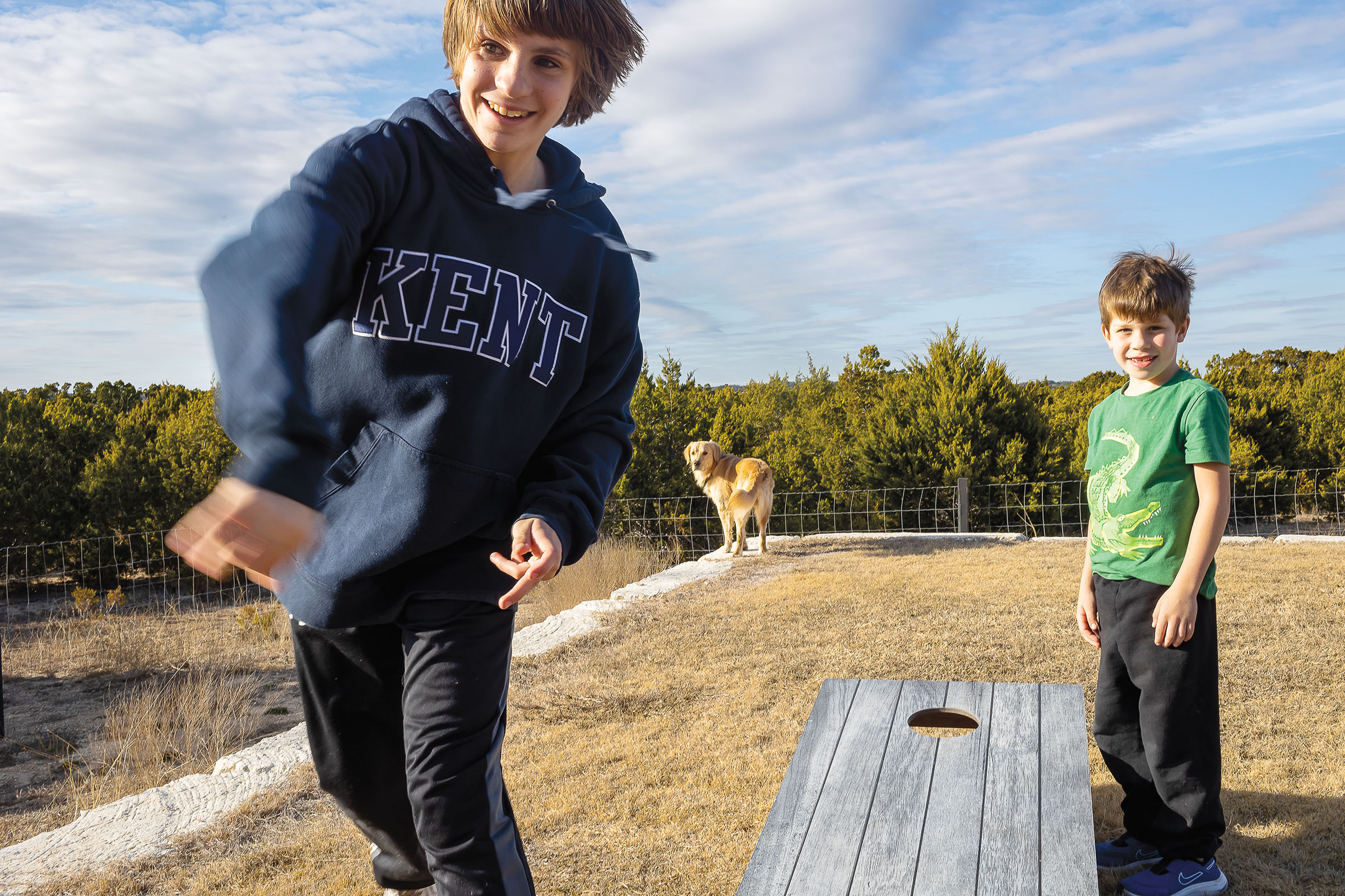 A picture of two young men playing cornhole with a golden retriever in the background