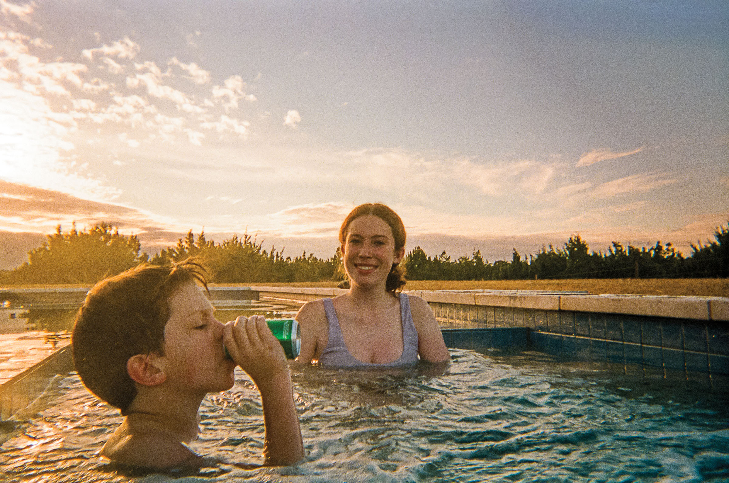 A young man and woman relax in a hot tub under a Hill Country sky. The young man drinks a soda.