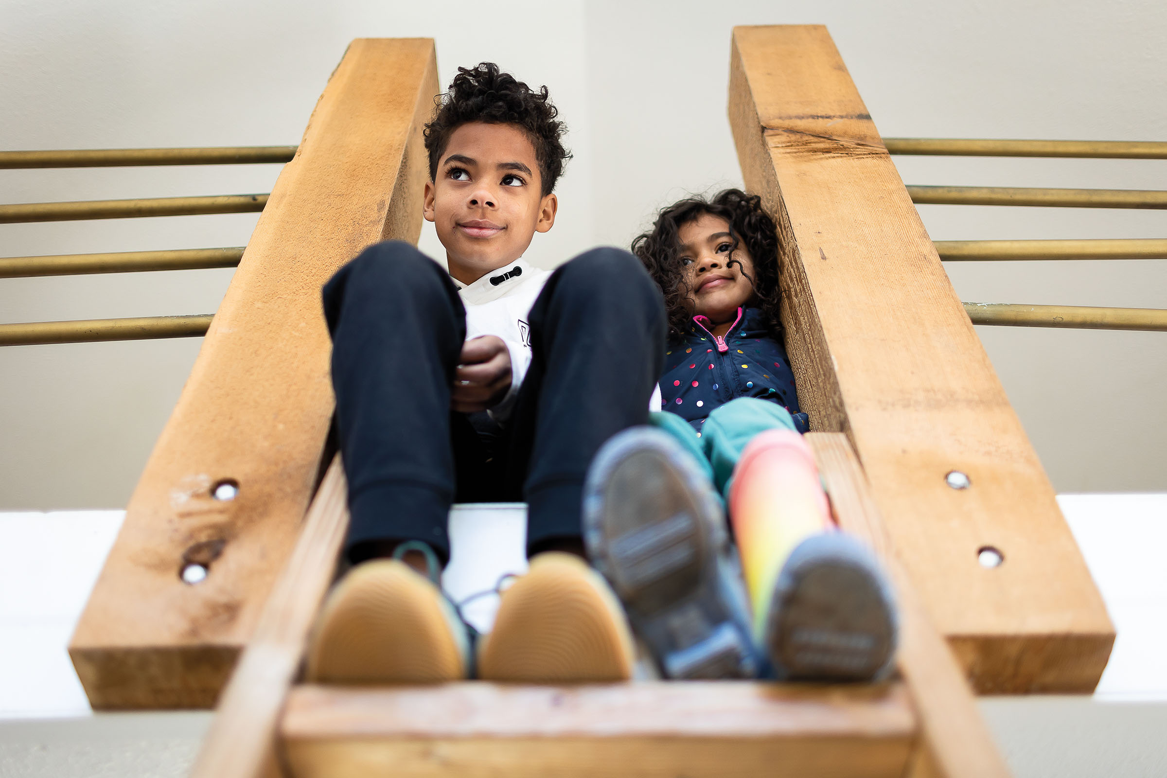 Two children smile slyly looking down from a bedroom loft