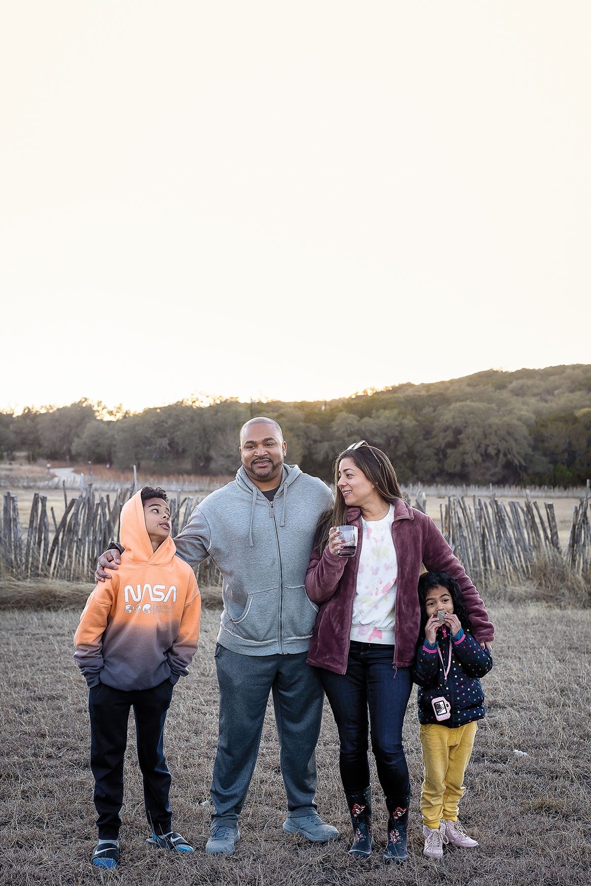 A group of four people stand in a Hill Country landscape in an orange sunset
