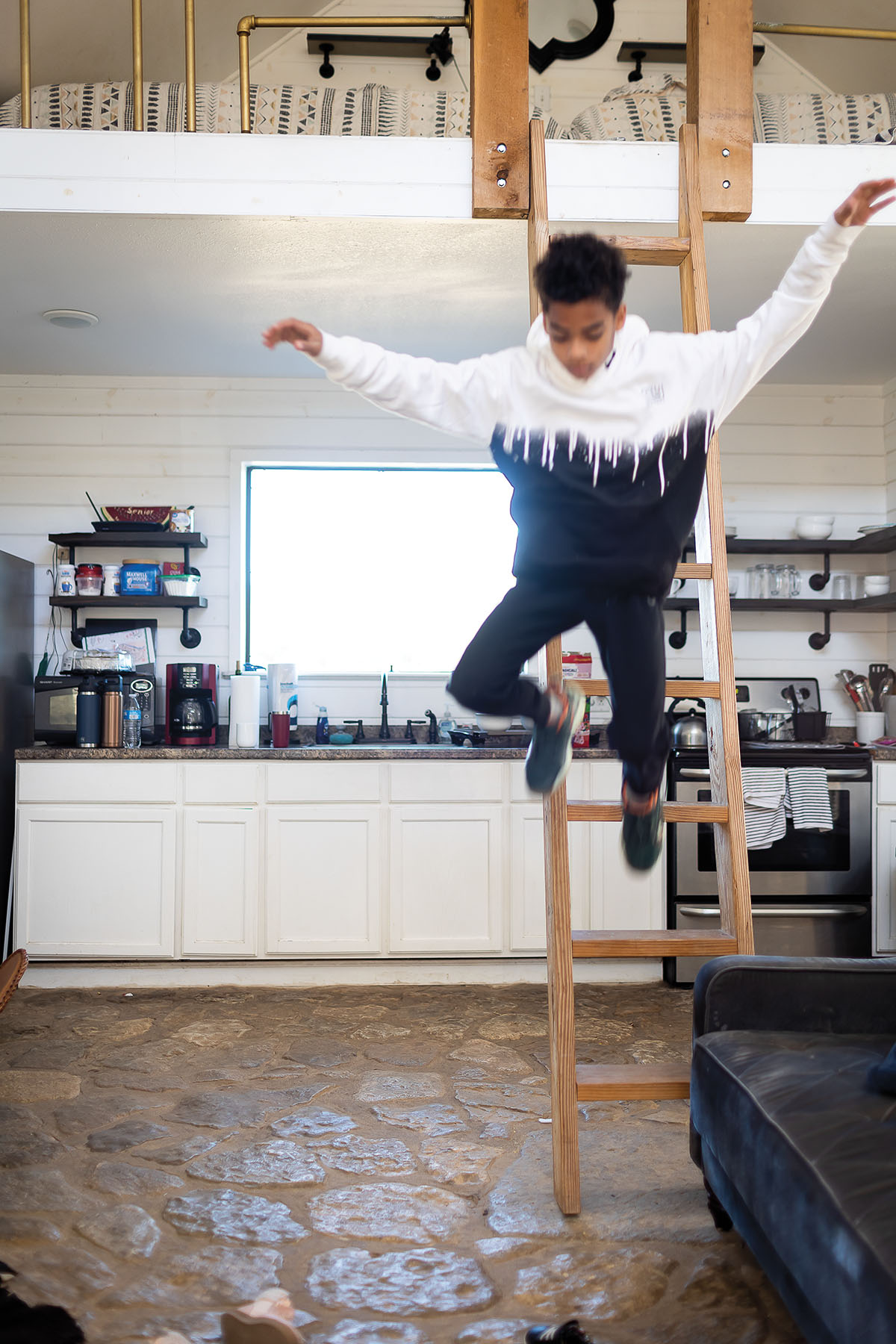 A yoiung man jumps down a wooden ladder from a bedroom loft