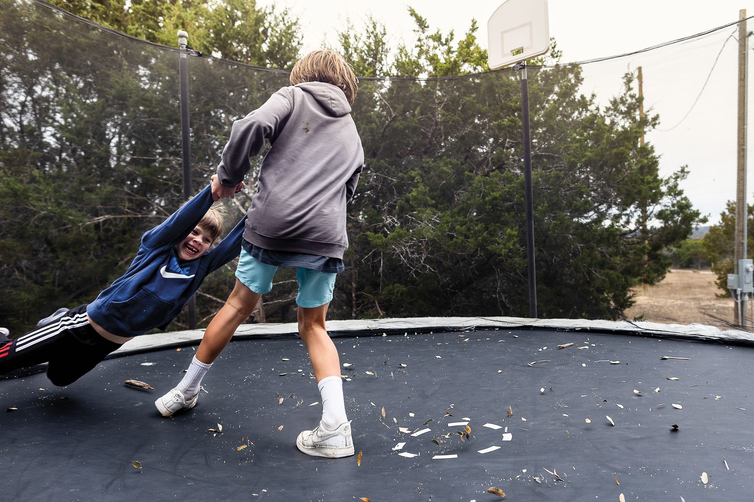 A picture of a young man swinging another young man around on a trampoline