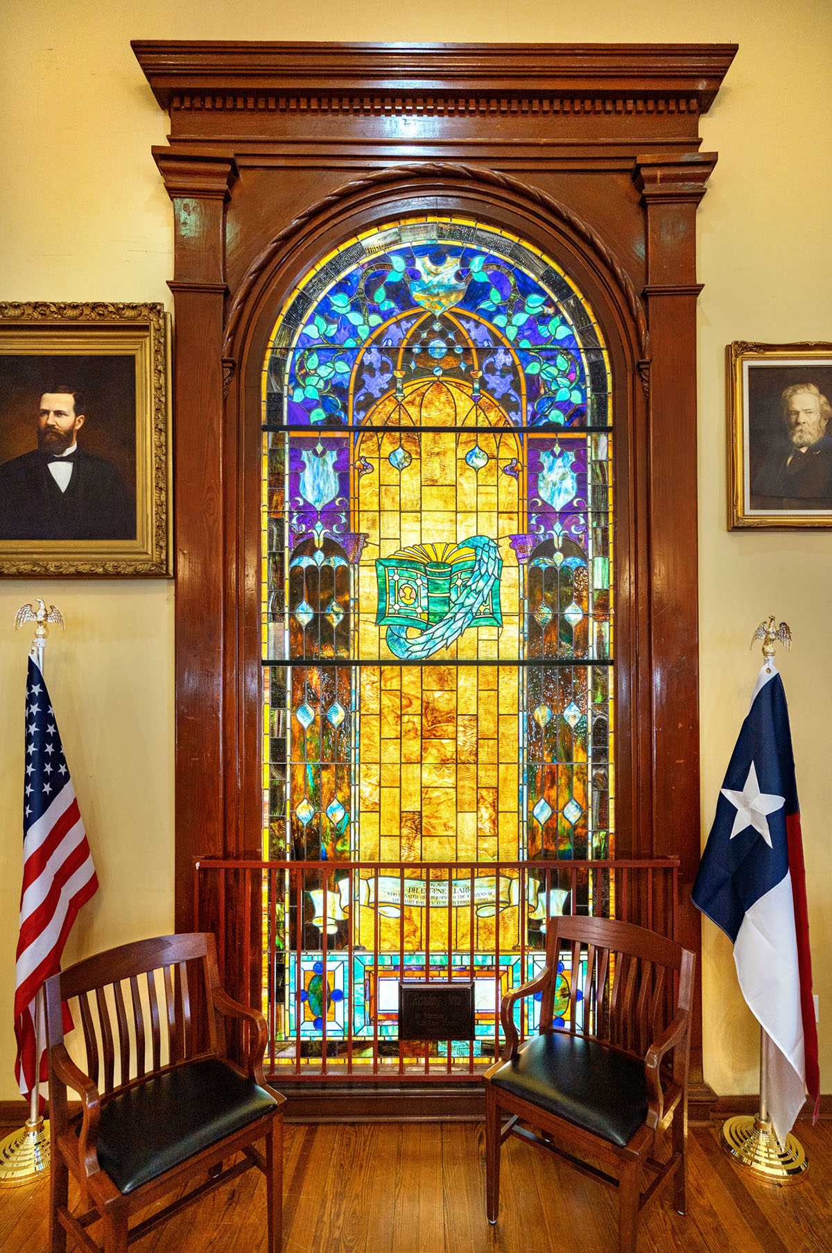 A stained glass window behind United States and Texas flags