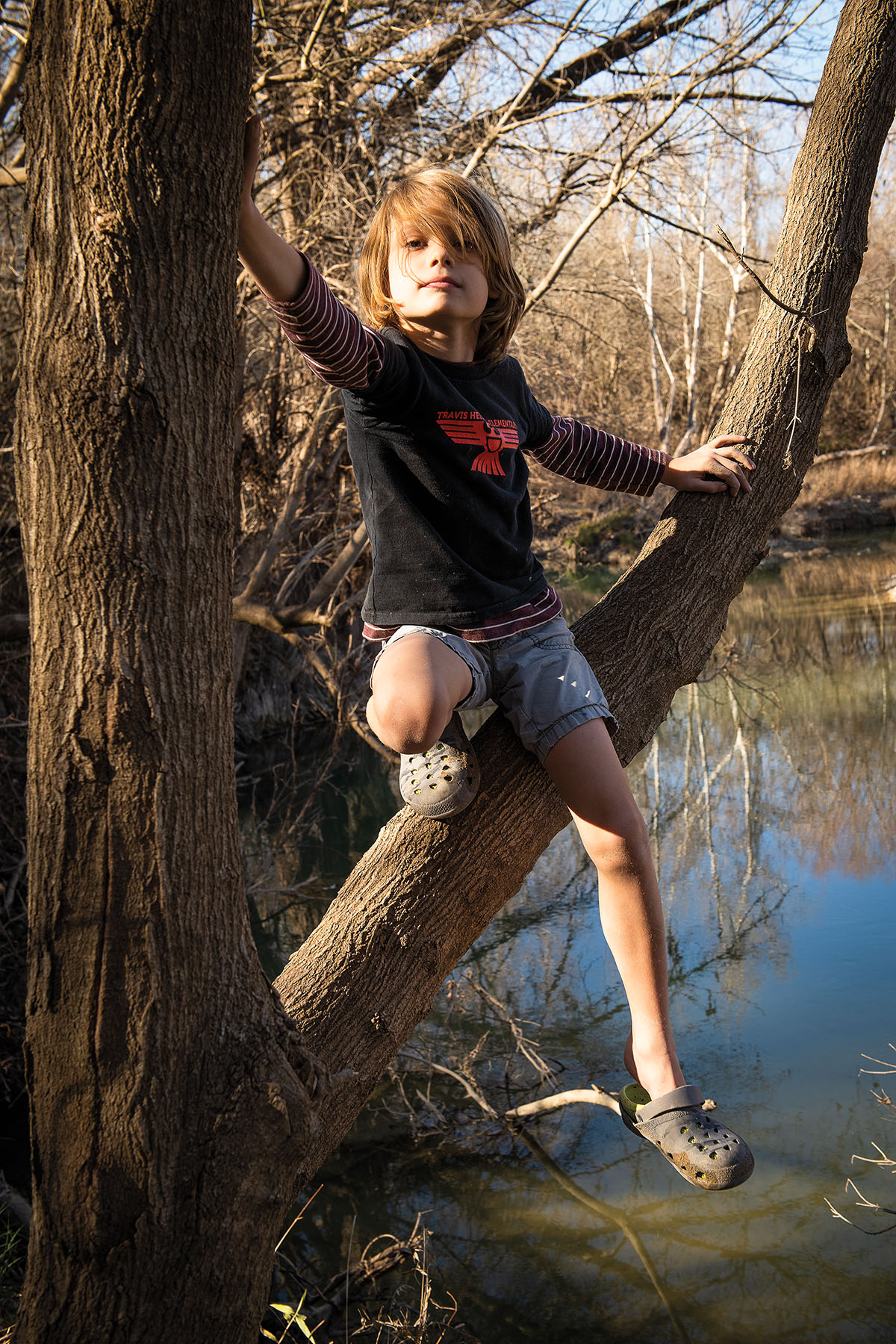 A young person sits on a tree over still water