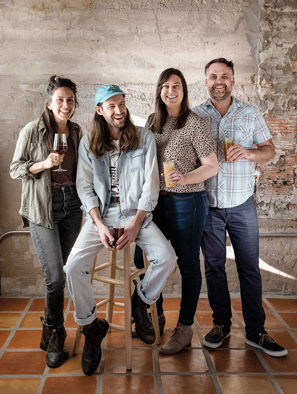 A group of people stand smiling and holding drinks in front of an exposed stone wall