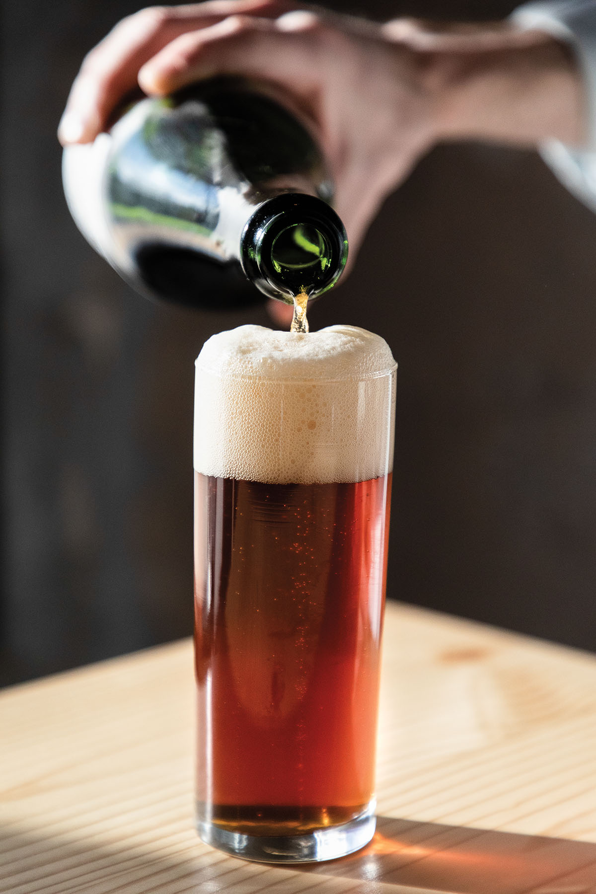 A bright red-brown beer is poured into a tall glass from a green bottle