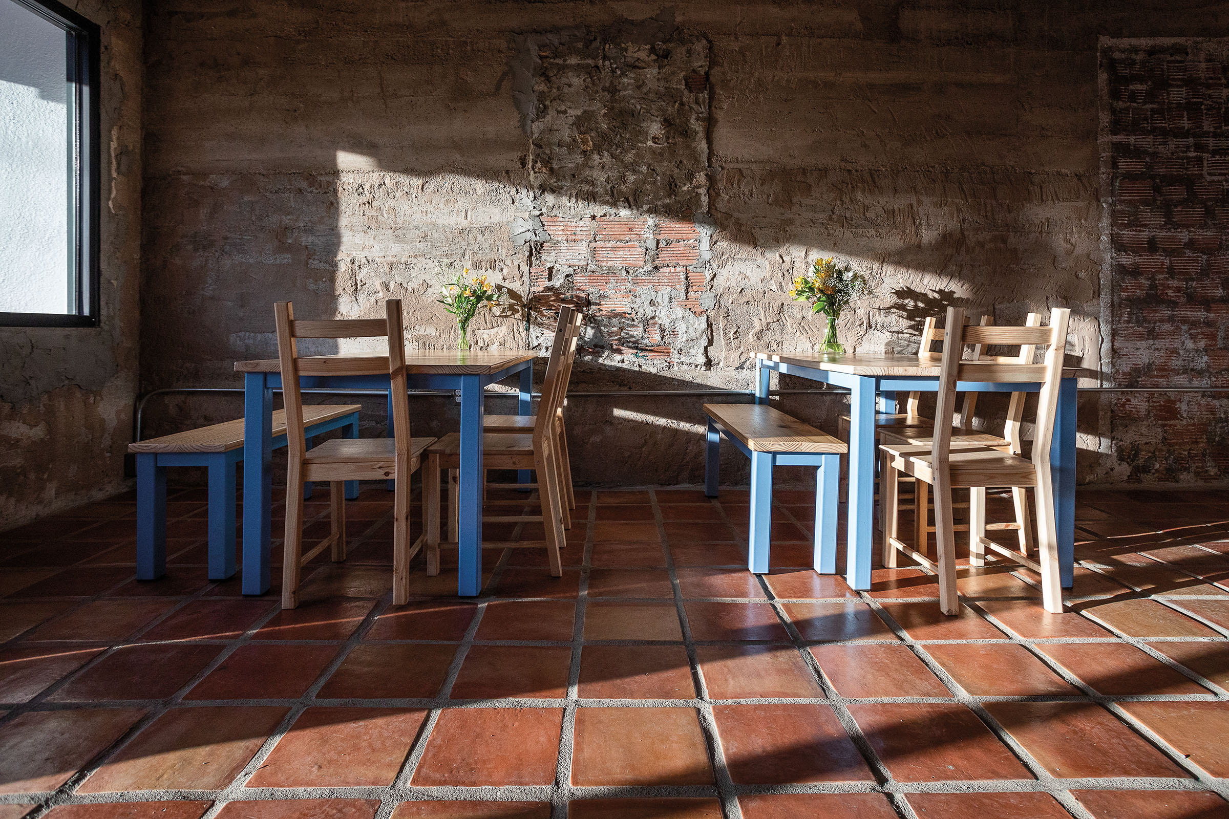 Wooden chairs and tables on a red brick floor in front of a stone wall