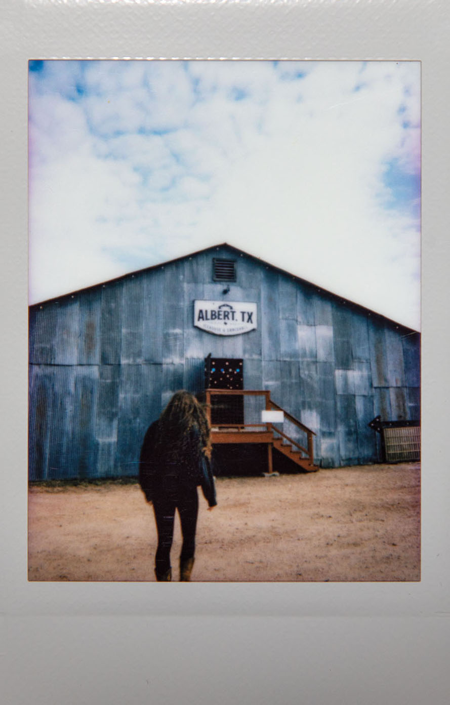 A Polaroid picture of a woman walking up toward a metal-sided building reading 