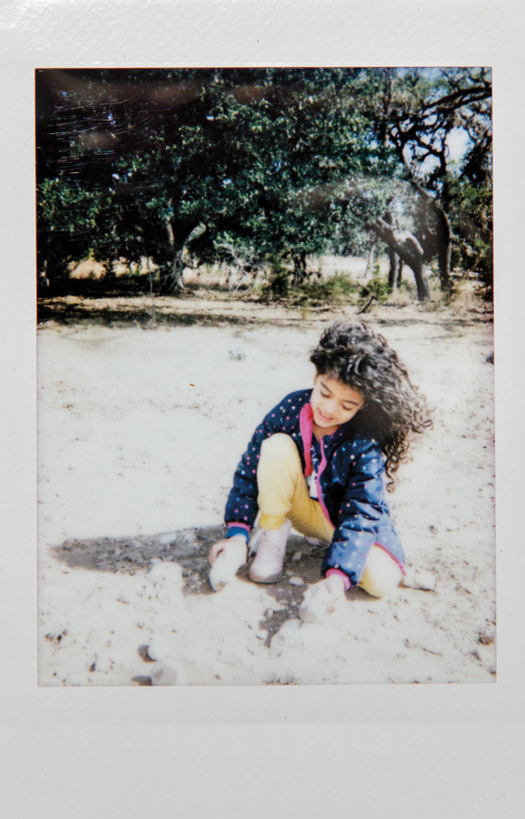 A Polaroid picture of a young woman crushing rocks together underneath a canopy of trees
