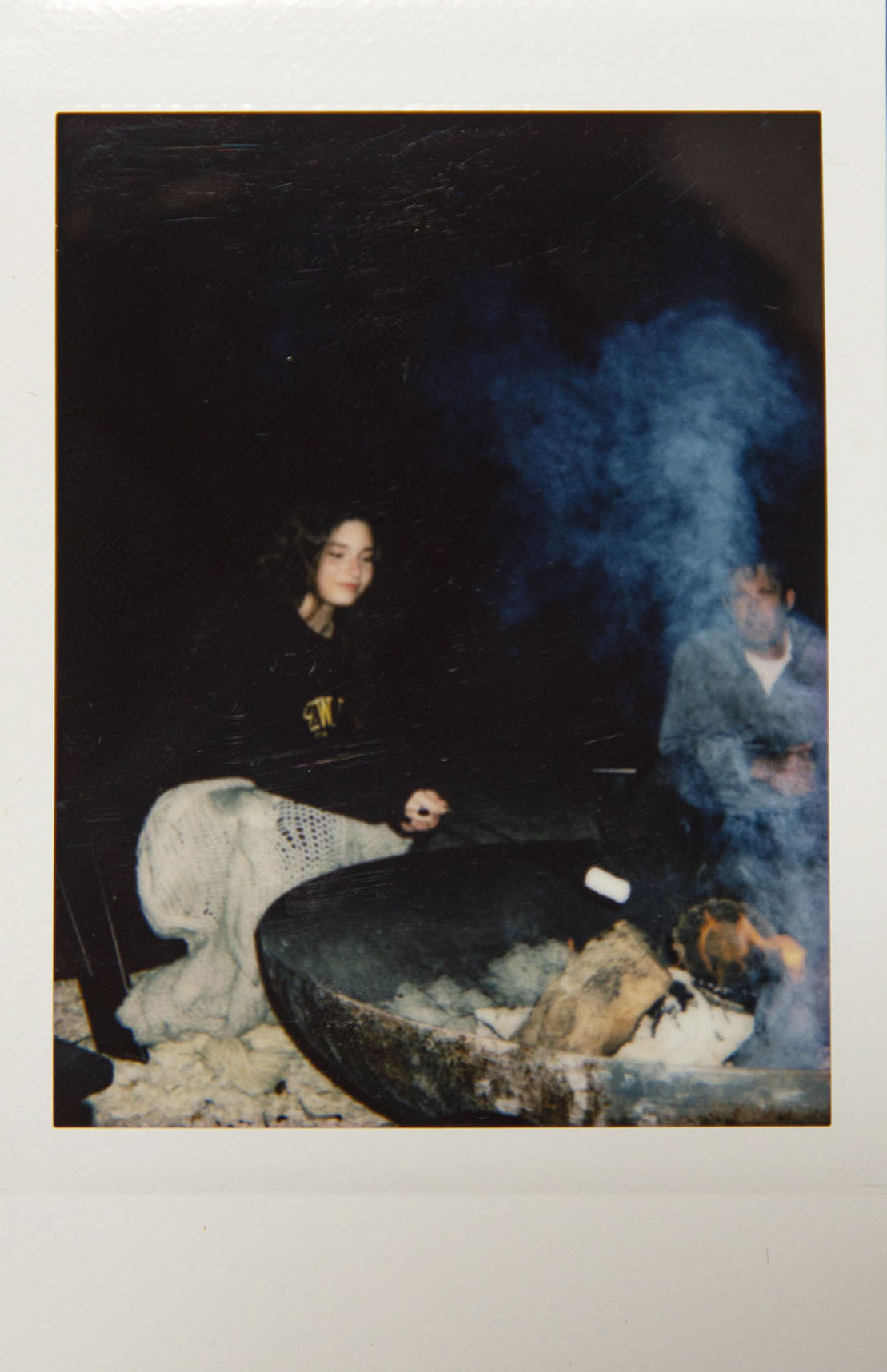 A young woman sits in the smoke of a campfire