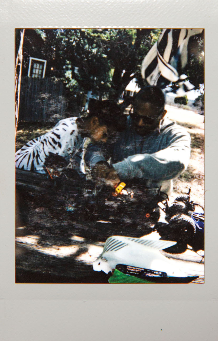 A Polaroid picture of a man and a young man working on an RC car in an outdoor setting