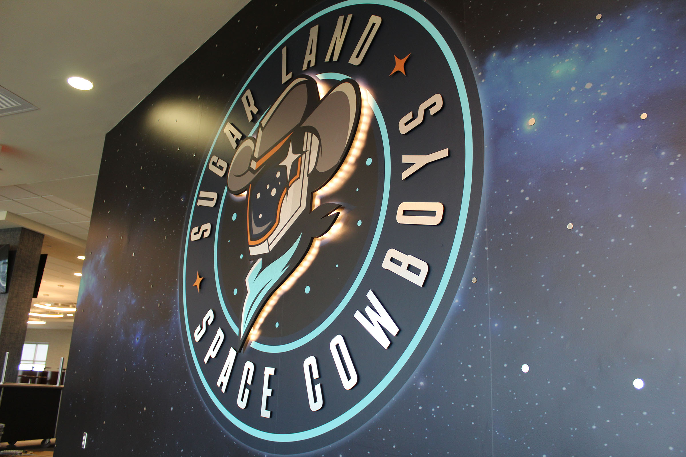 A picture of a large logo on a wall decorated with a space and stars image reading "Sugar Land Space Cowboys"