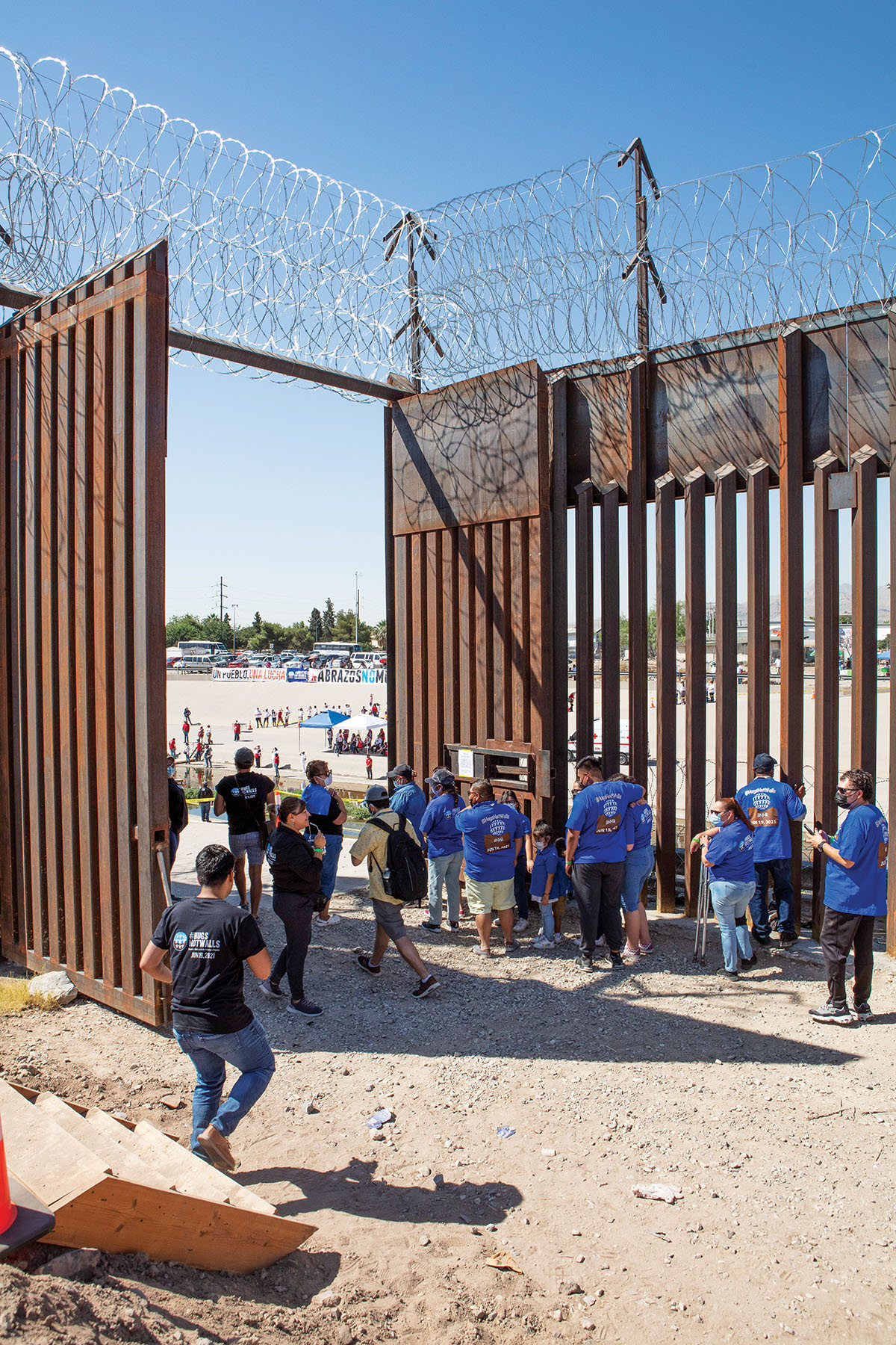 People line up to walk through an opening in a large fence under a blue desert sky