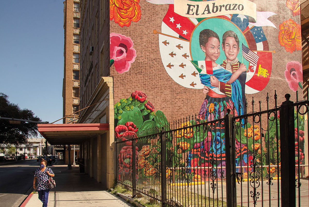 A woman walks down the street near a mural reading "El Abrazo"