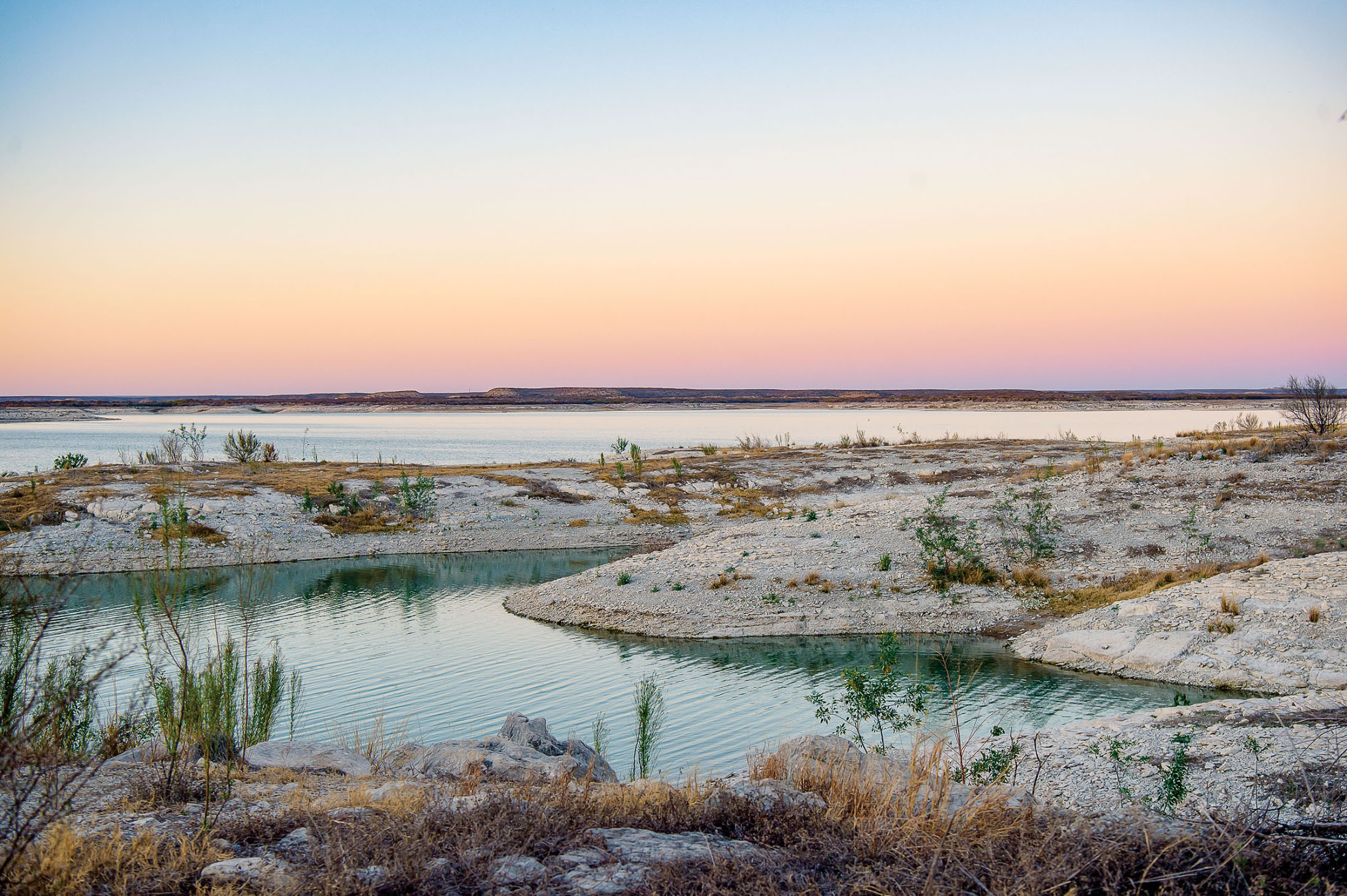 A purple, blue and gold sunset over the gray banks of Amistad Reservoir