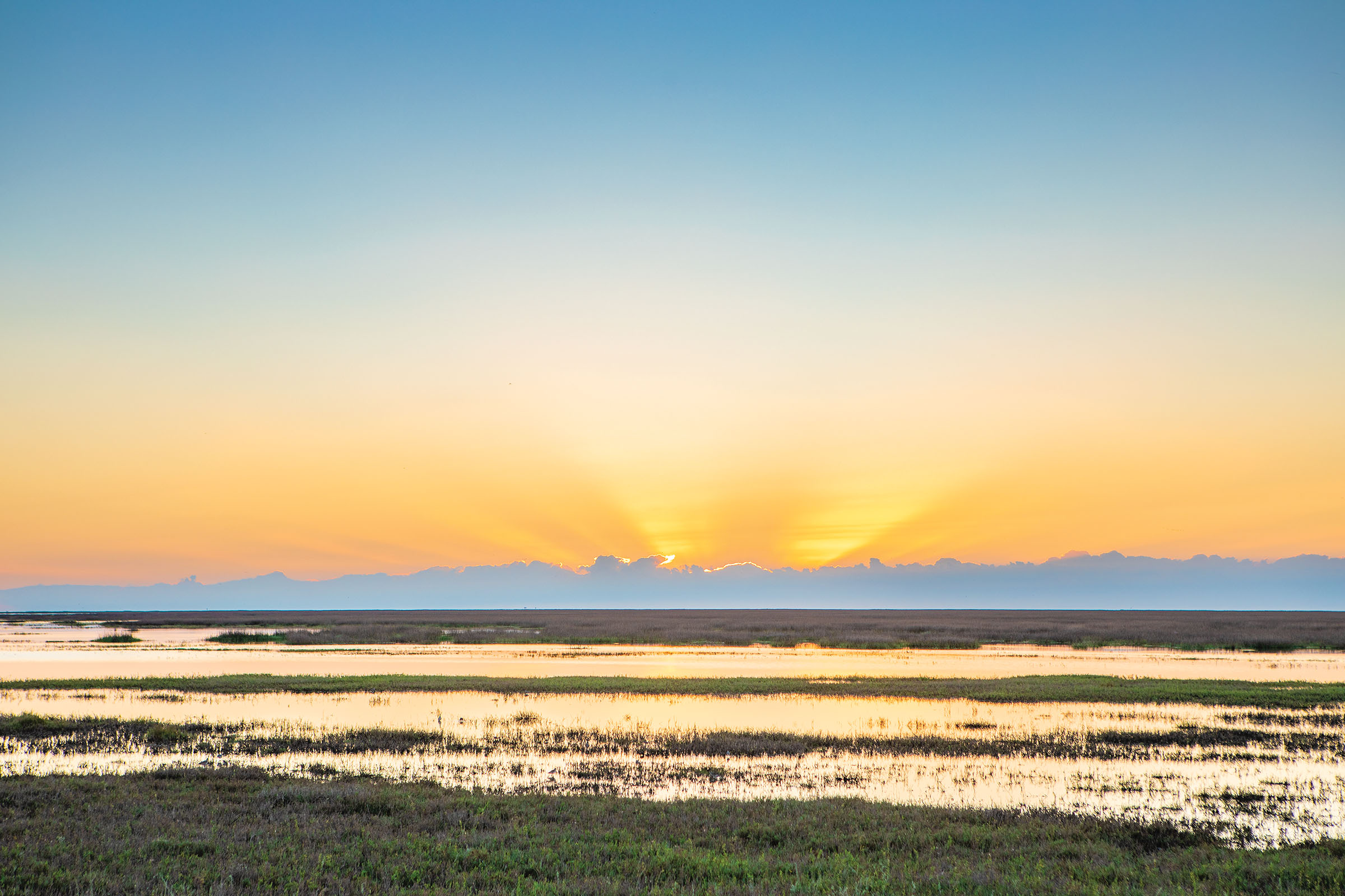 A bright golden sunrise over dark blue clouds and clear water