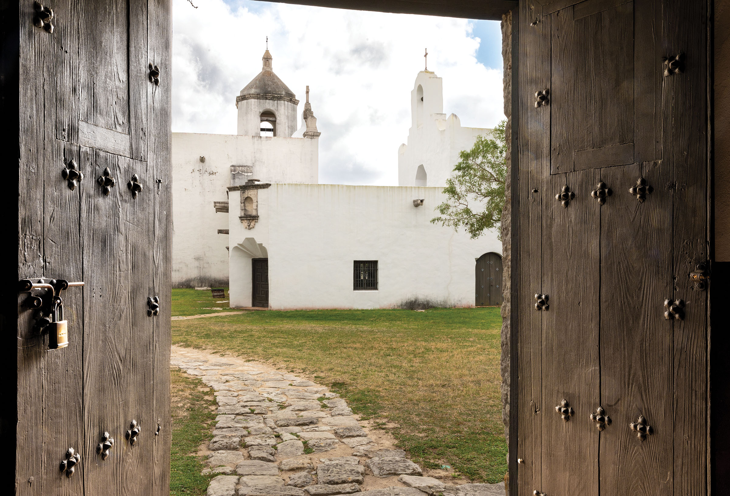 A white adobe building seen through the opening in a large wooden and iron door