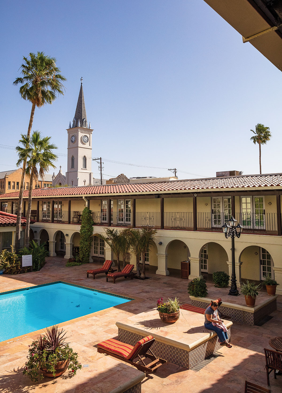 A cathedral is visible in the background of a two-level hotel with a bright blue pool