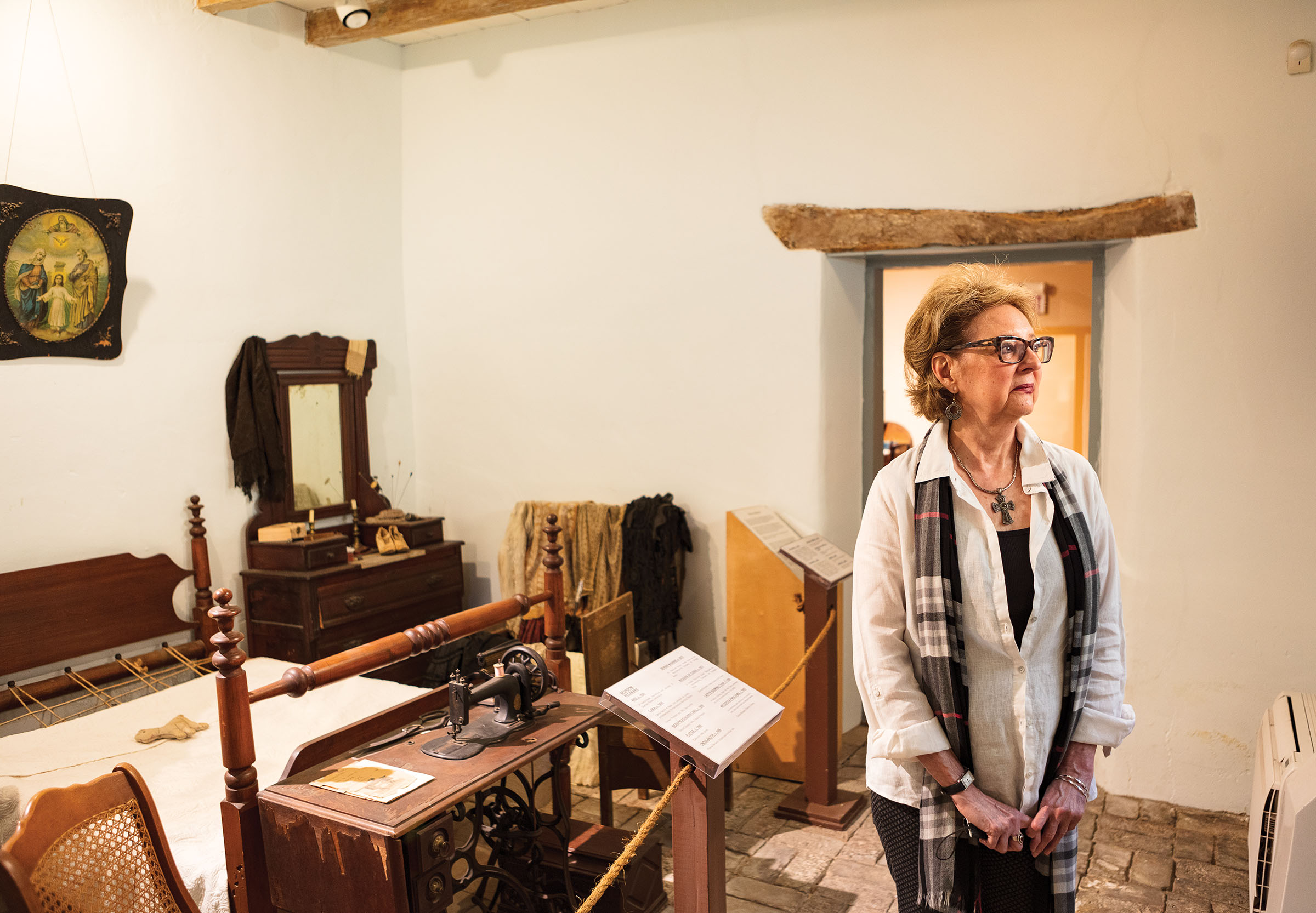 Awoman stands in a room filled with wooden antique furniture