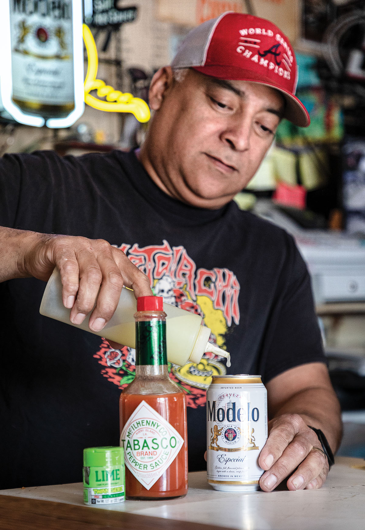 A man in a red baseball cap pours lime juice into a small can of Modelo