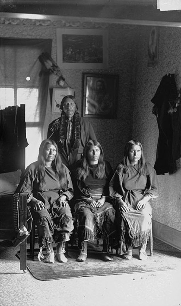 Comanche leader Quanah Parker poses for an image with three of his wives seated in front of him.