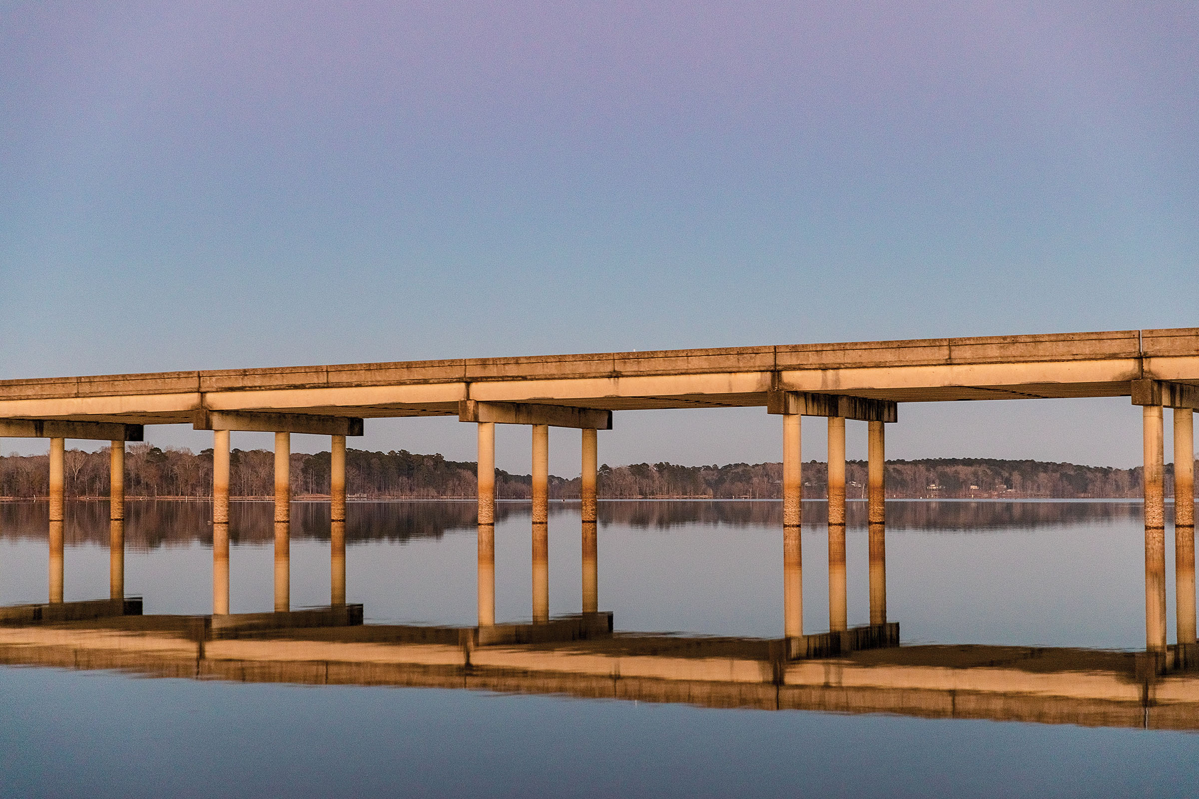 A concrete bridge spanning a perfectly flat body of  waternear low hills