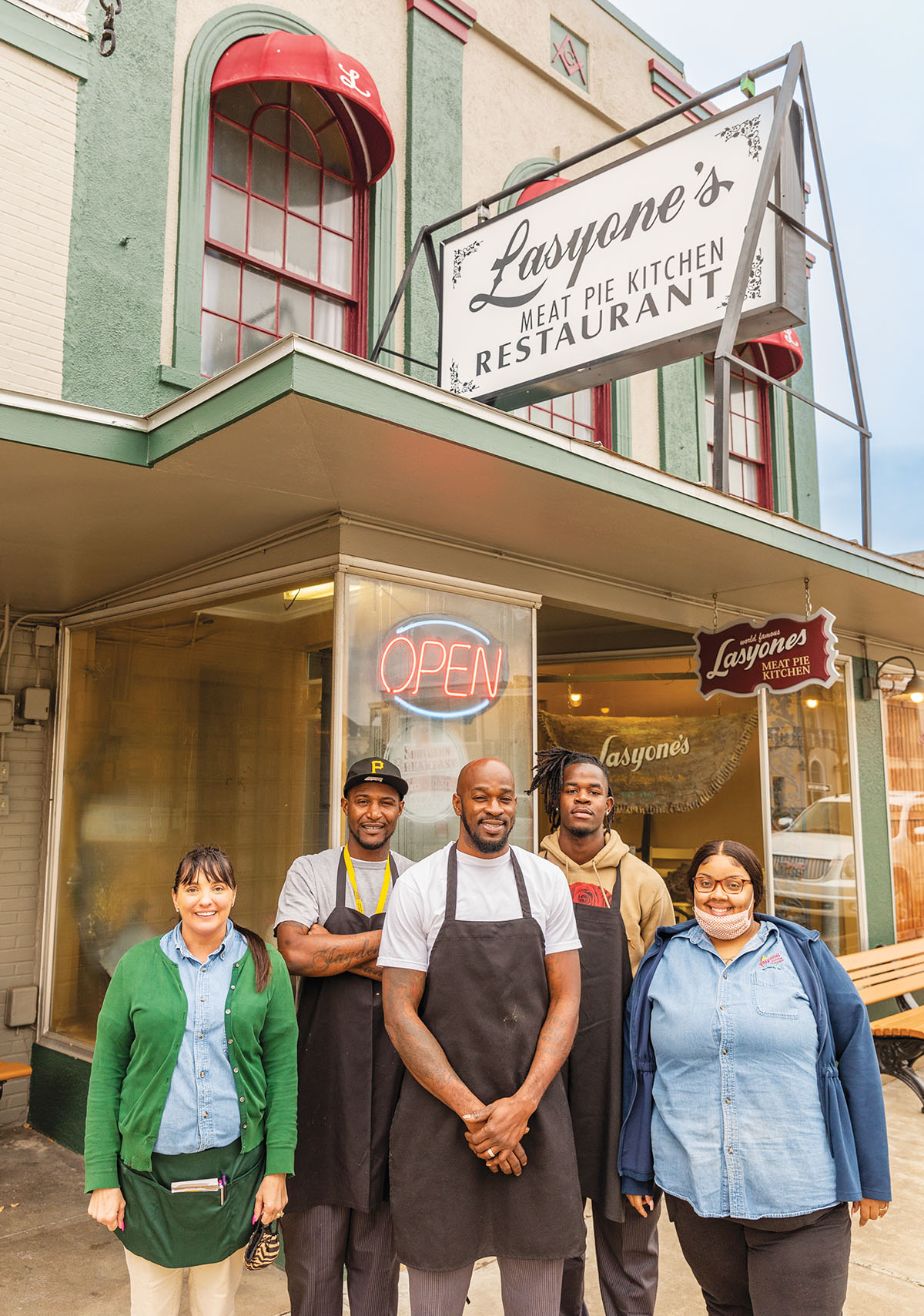 A group of peolestand in front of a restaurant with a sign reading "Lasyone's Meat Pie Kitchen Restaurant"