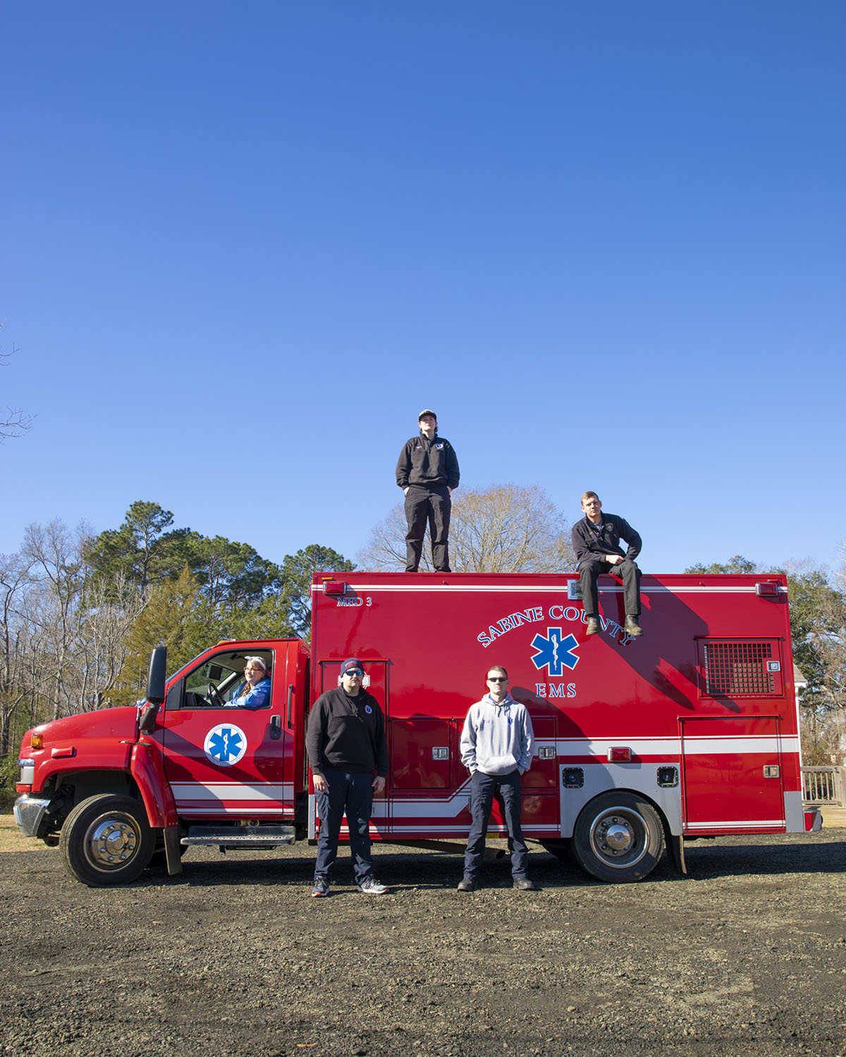 A group of people stand on and around a red ambulance