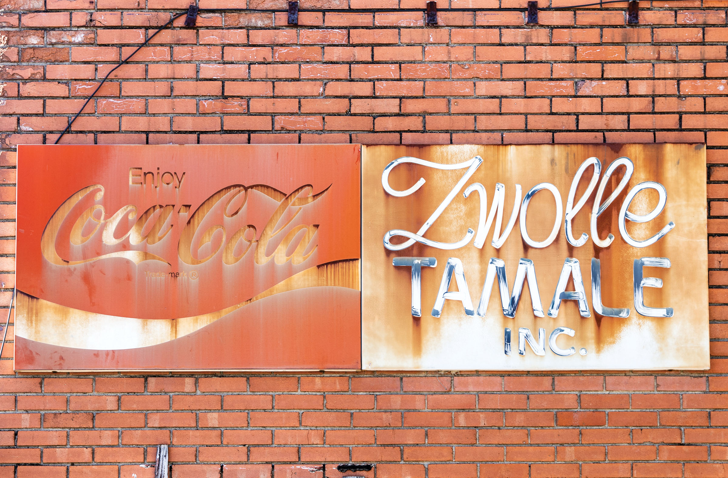 A rusted sign on a brick wall reading "Coca Cola" and "Zwolle