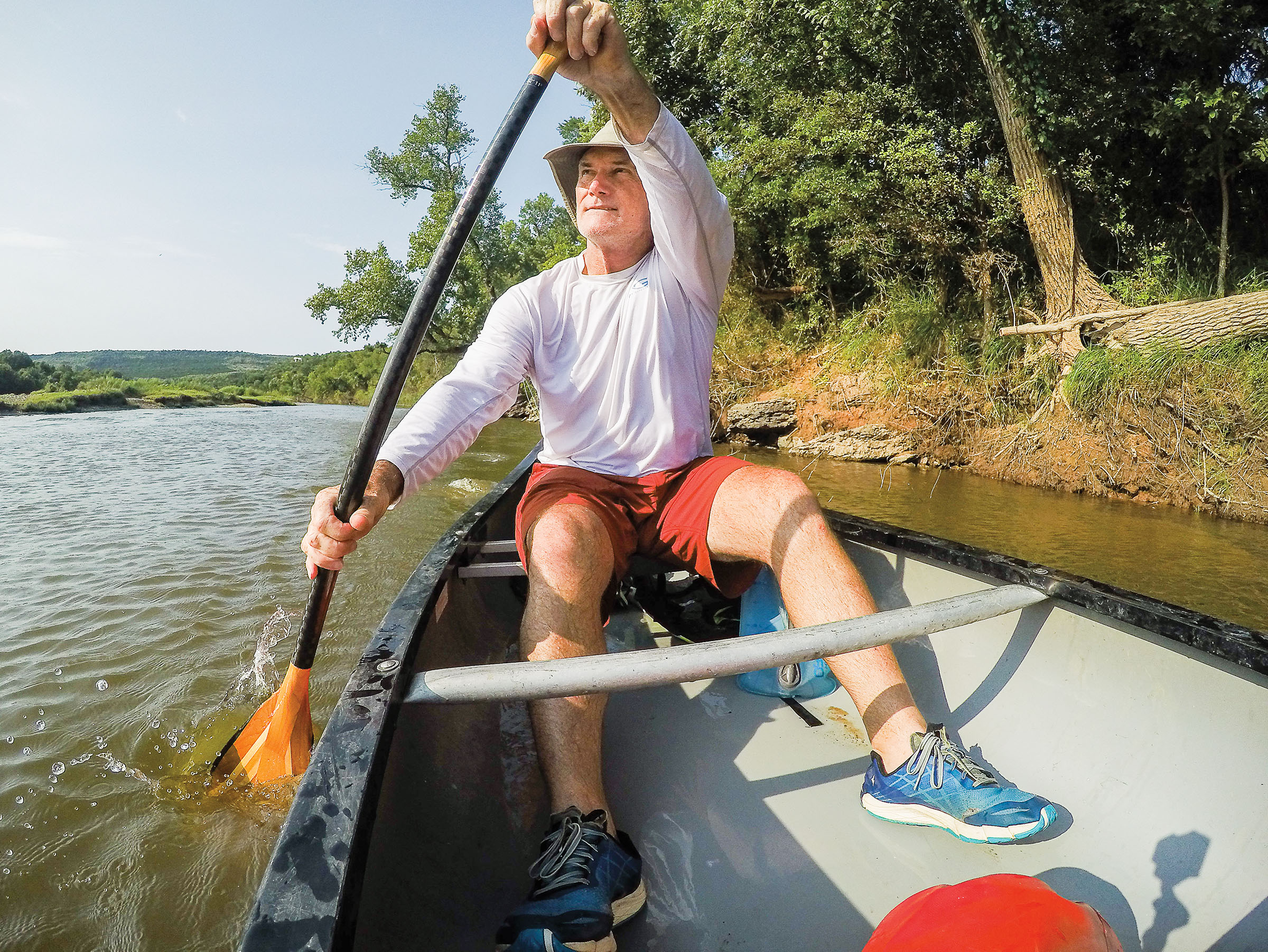 A man in a long-sleeve white shirt paddles a canoe