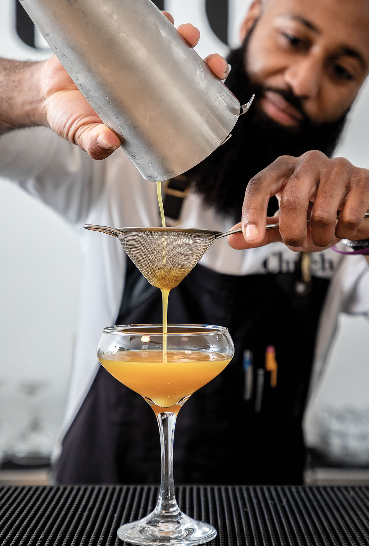 A man pours an orange-colored cocktail from a silver shaker