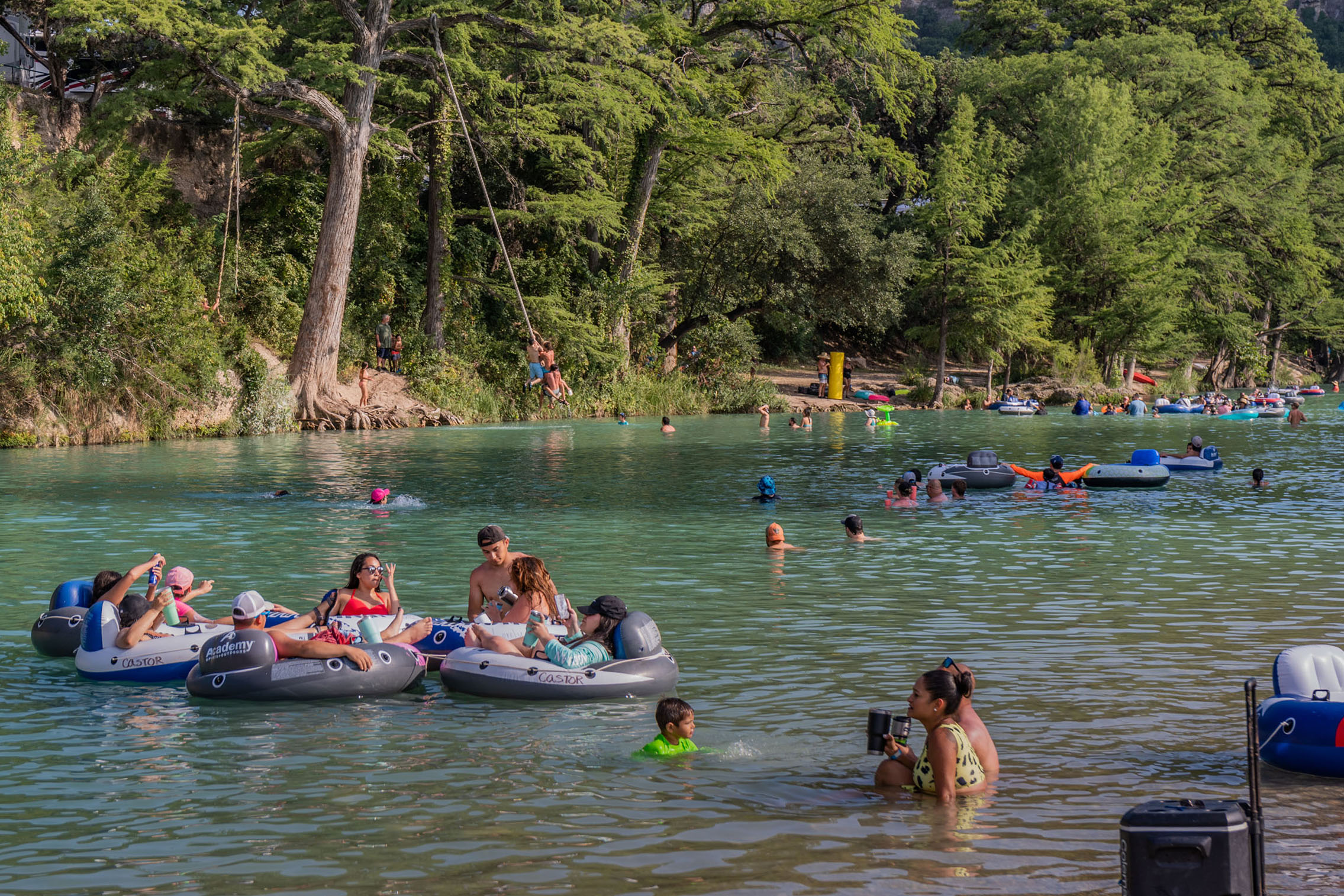 Large groups of people float, wade, and swing into the Frio river in Garner State Park