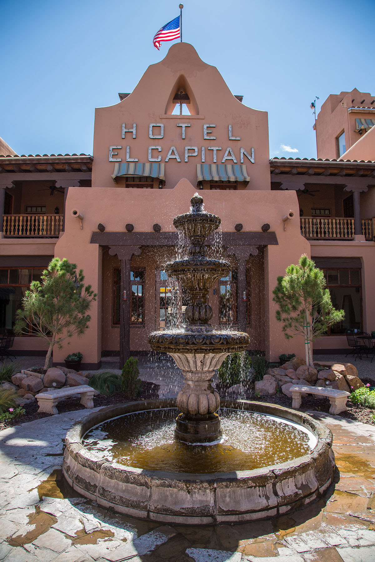 The exterior of a red adobe hotel with a sign reading 'Hotel El Capitan'