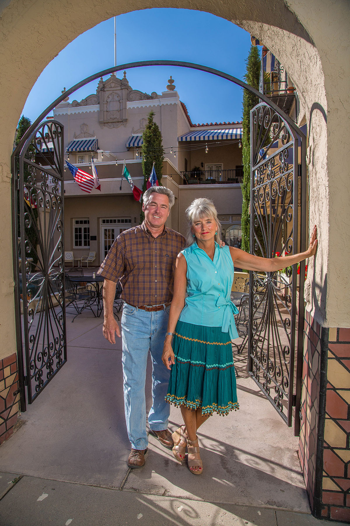 Two people stand in front of a gate outside of a tall hotel