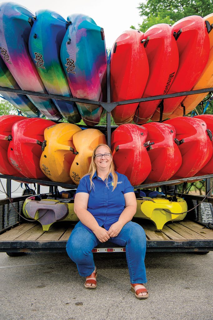 A woman sits at the end of a trailer full of brightly colored red, orange and blue kayaks