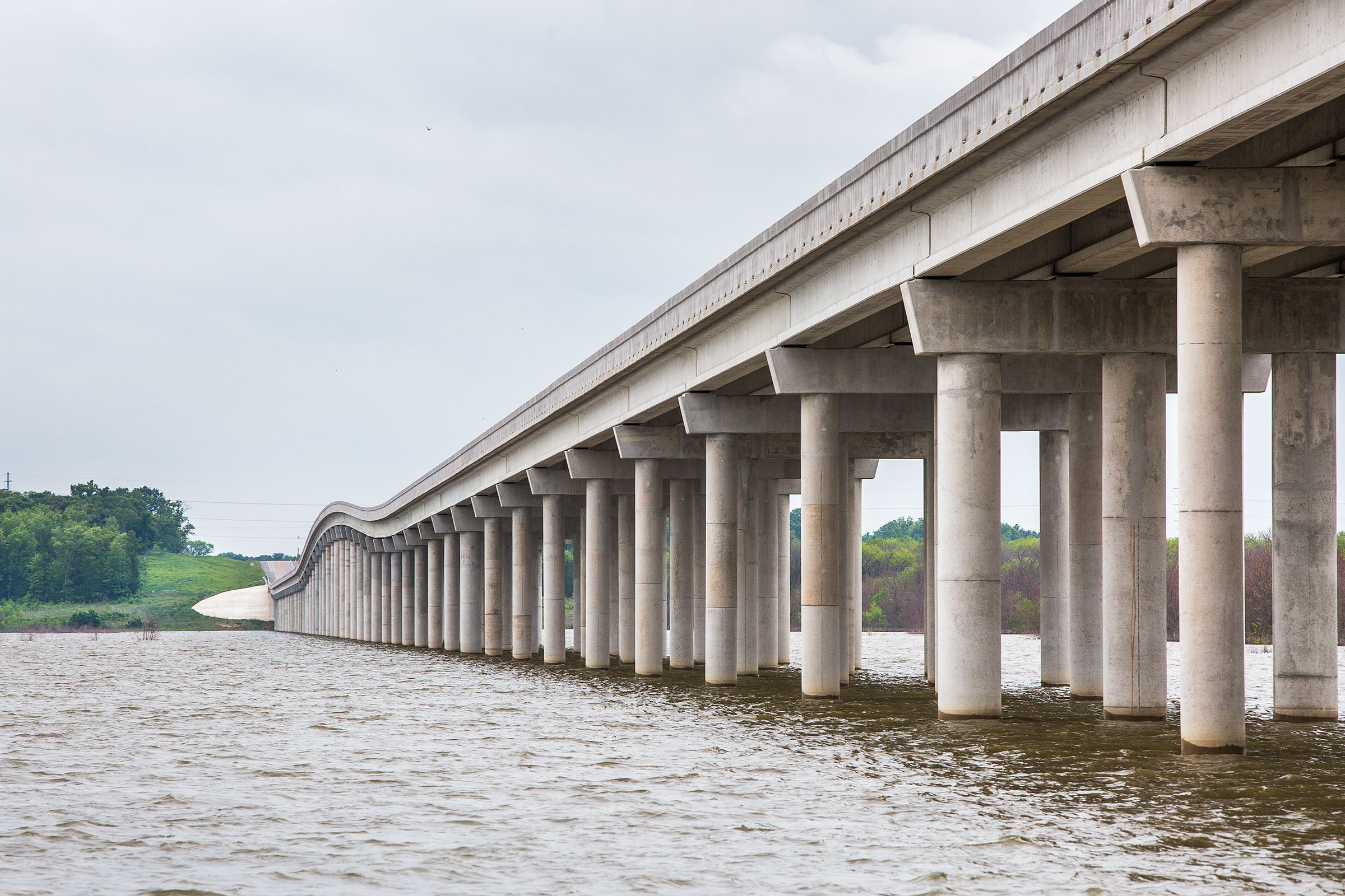A large concrete bridge spans over grayish water under gray skies