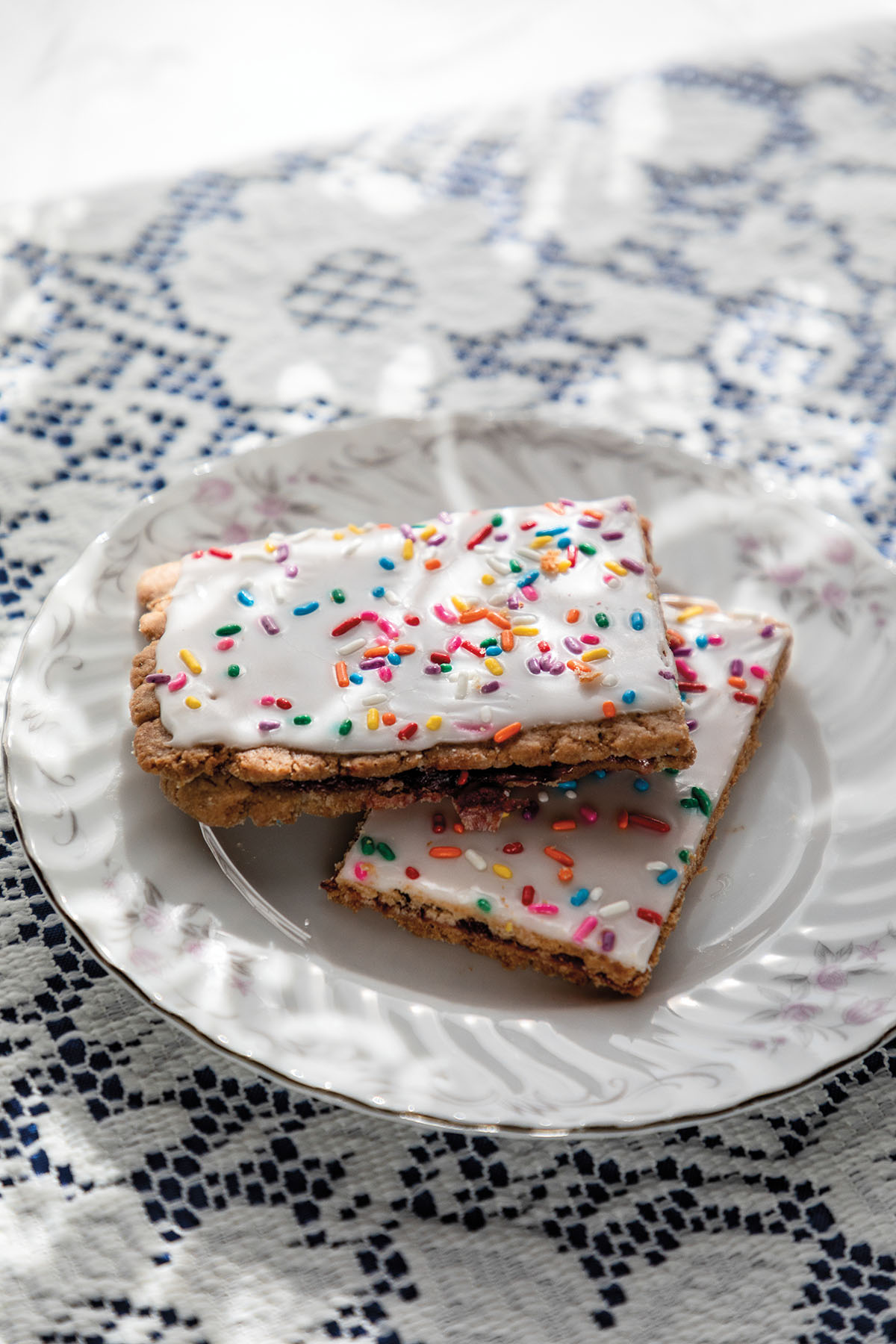 A pastry with white frosting and rainbow sprinkles on an ornate white plate