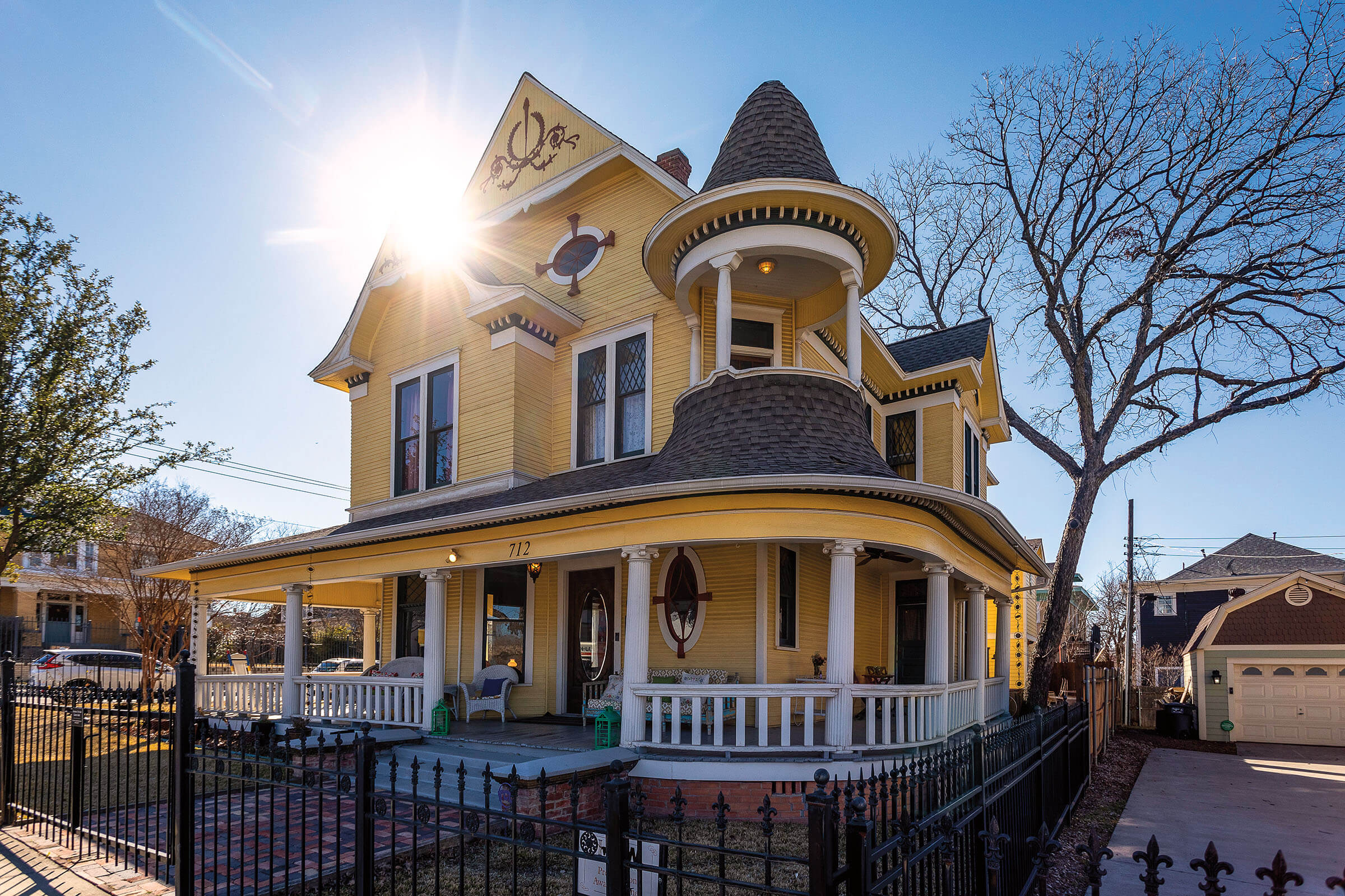 The exterior of a large, Victorian-style home painted yellow in the sunlight