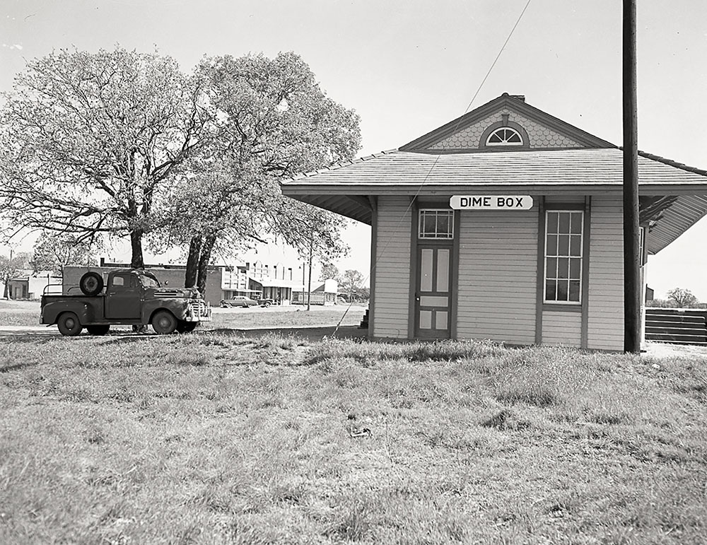 A black and white photograph of a stucco building with a small sign reading "Dime Box"