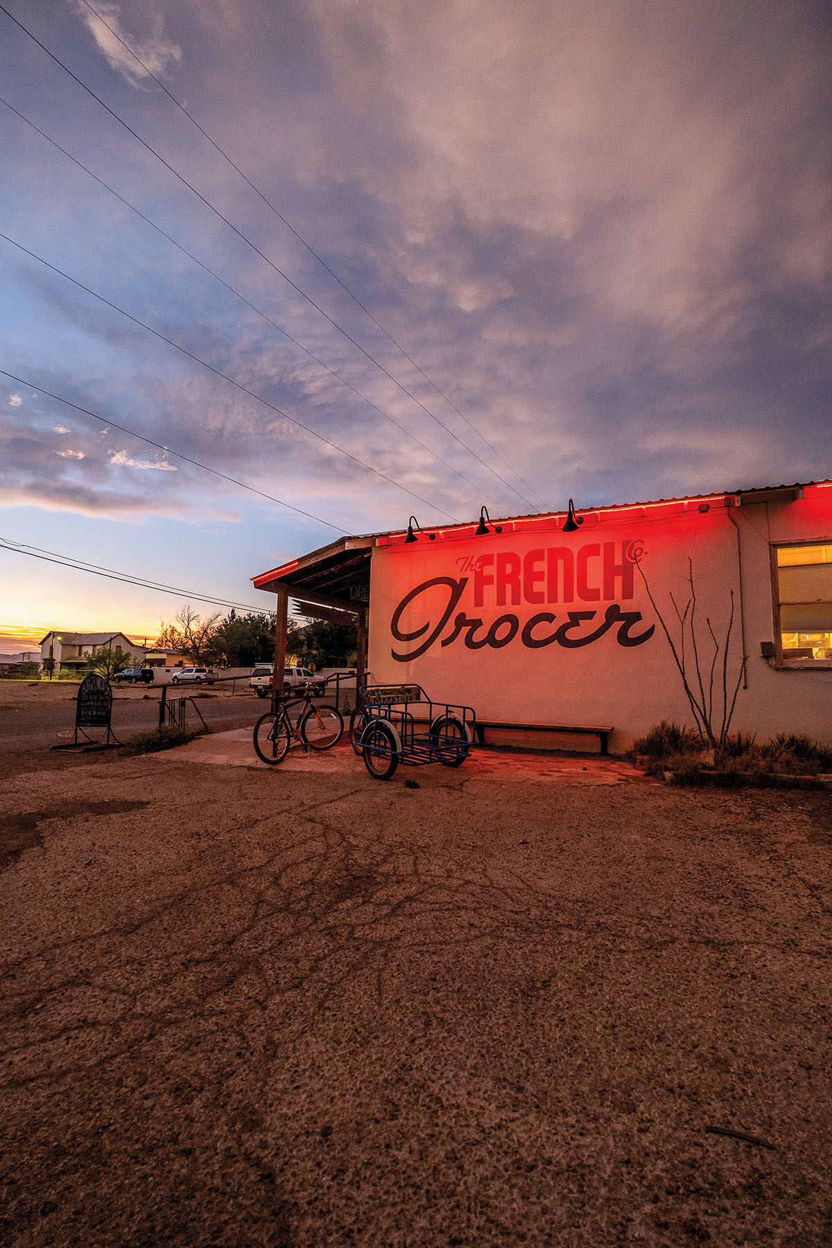 The exterior of a building reading "The French Grocer" doused in red light under an evening sky