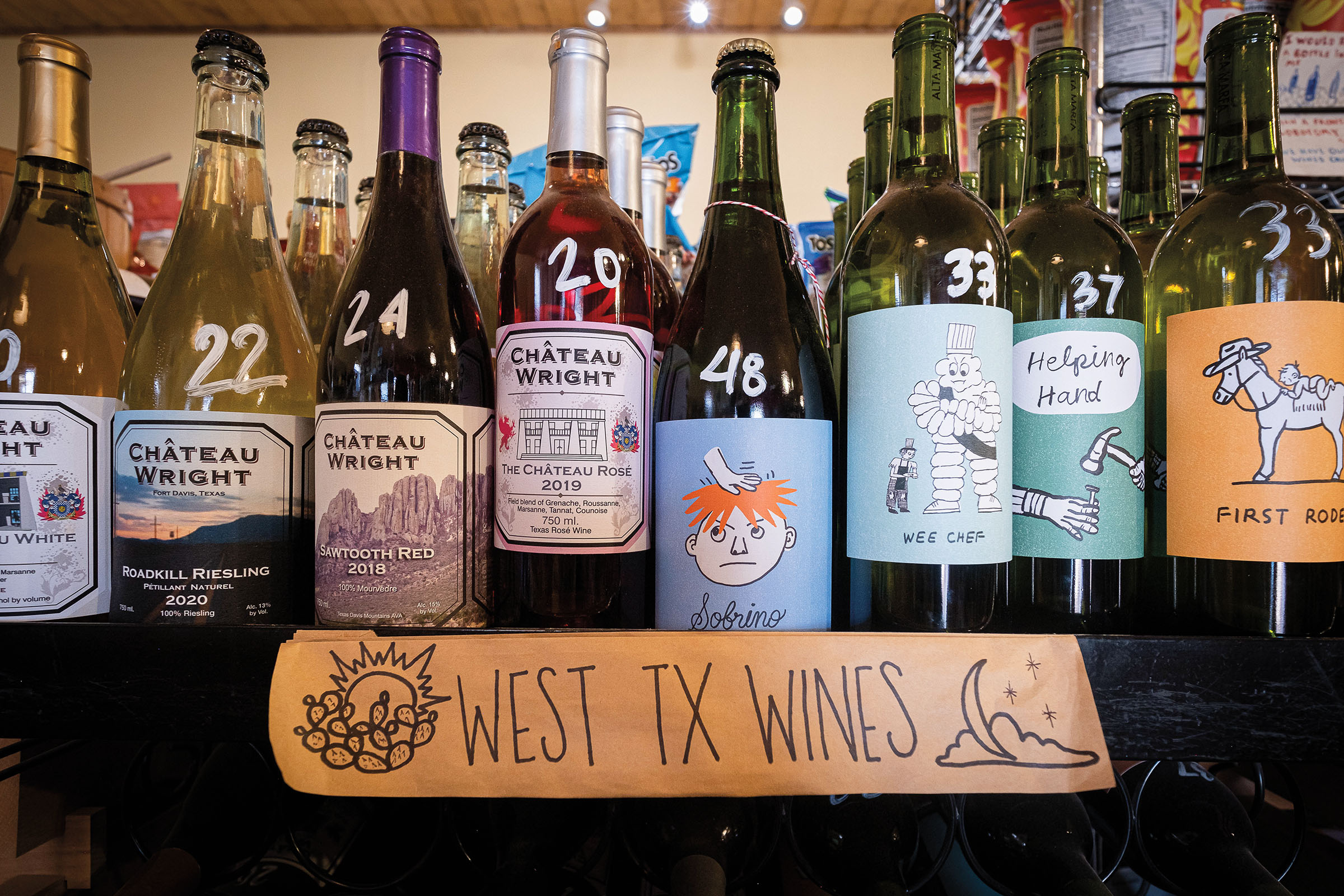 A collection of different color wine bottles behind a wooden sign reading "West TX Wines"