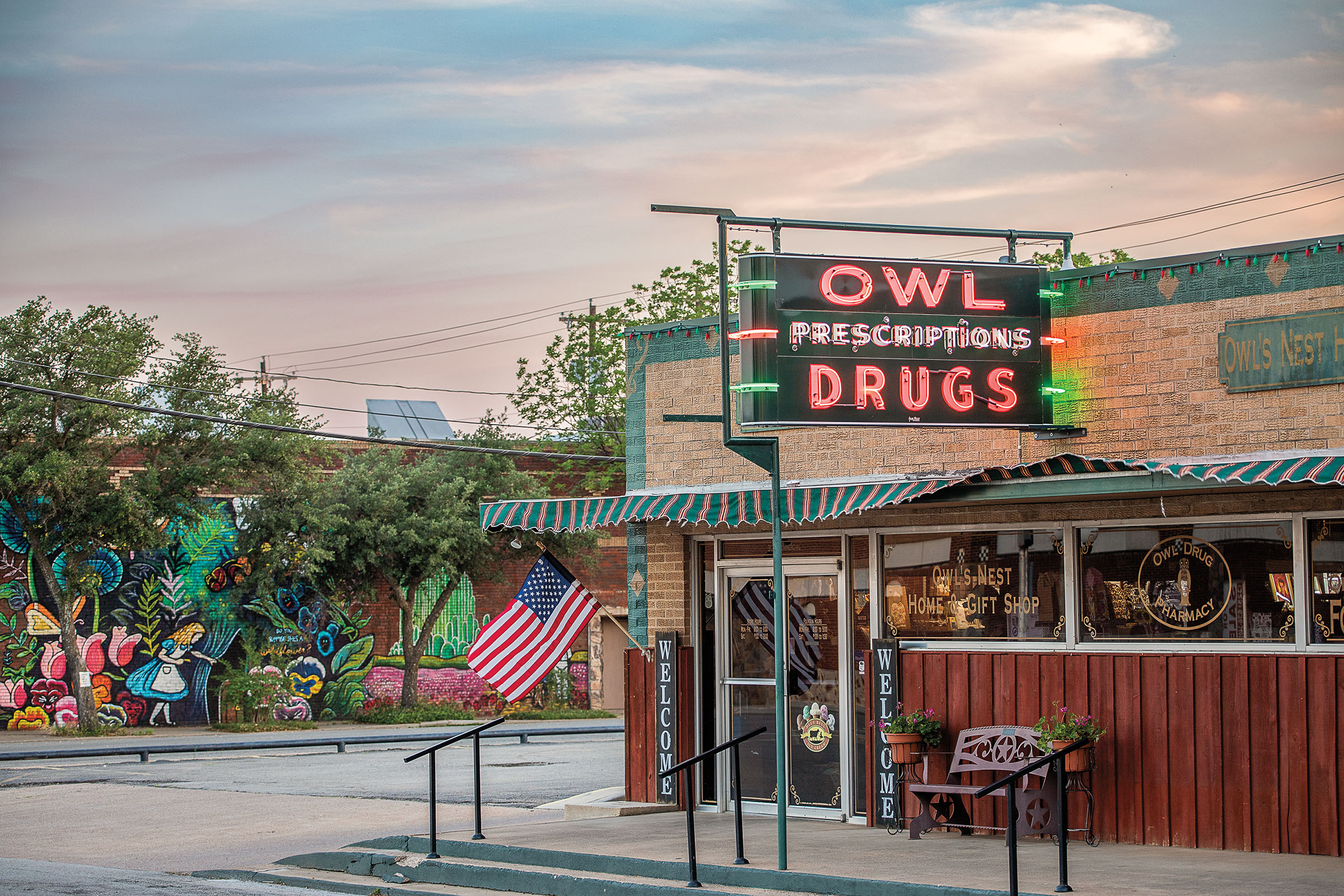 The exterior of a brick building with a neon sign reading "Owl Prescriptions Drugs"