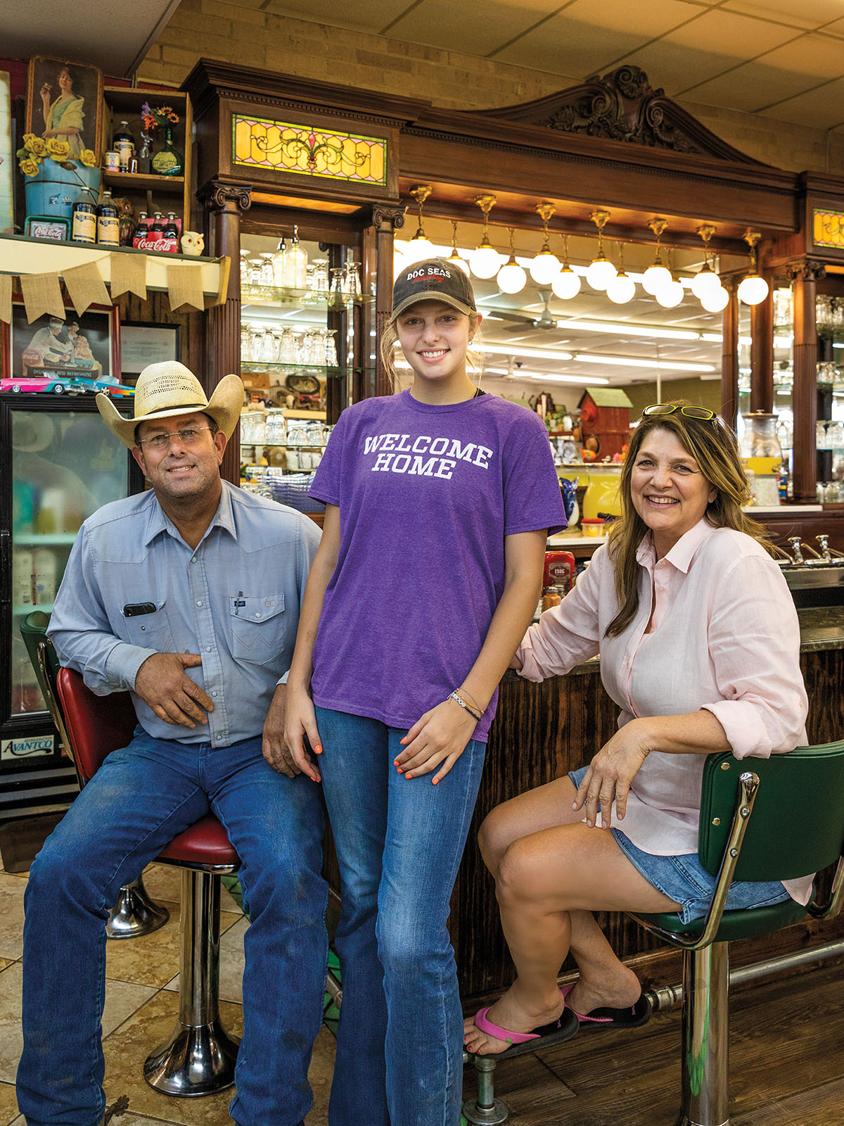 Three people lean on barstools in front of an old fashioned soda fountain