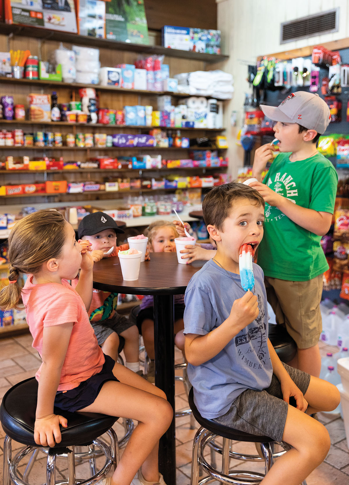 A group of children eat popsicles and other cold treats inside of a well-stocked store