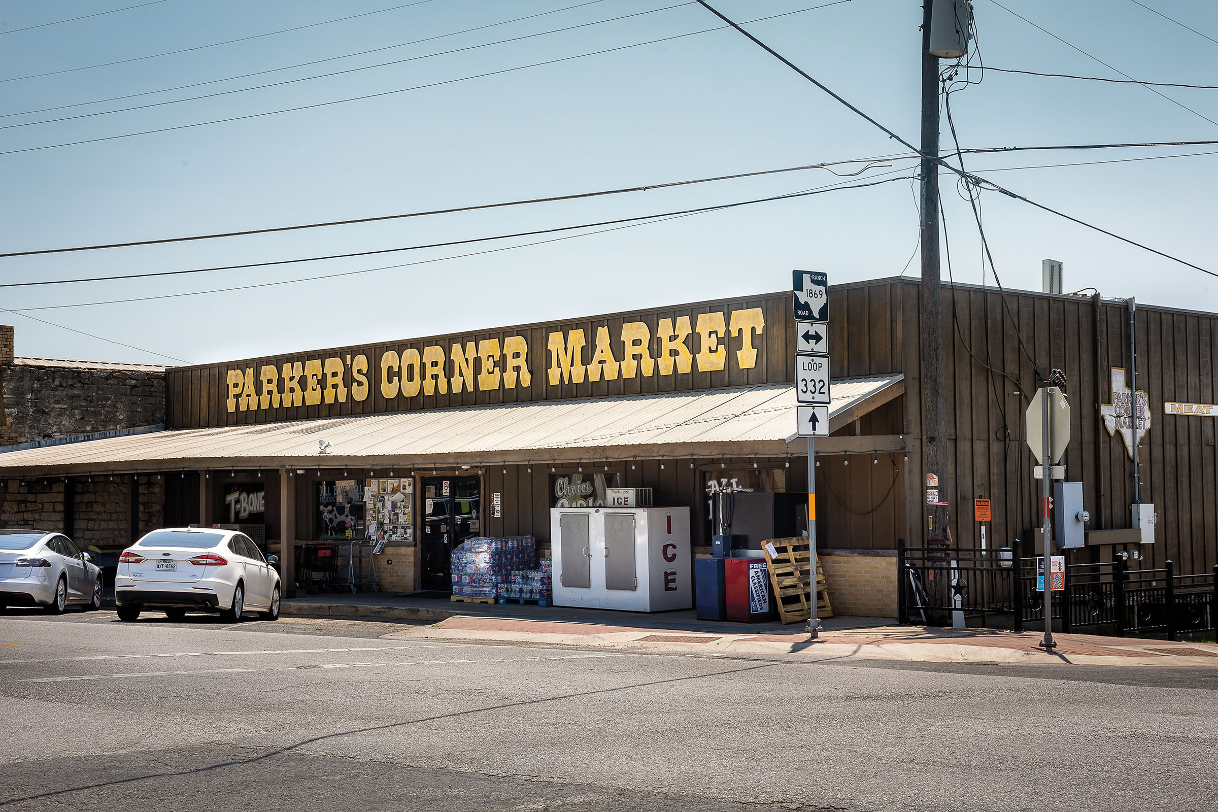 The exterior of a dark wood building reading Parkers Corner Market in yellow lettering
