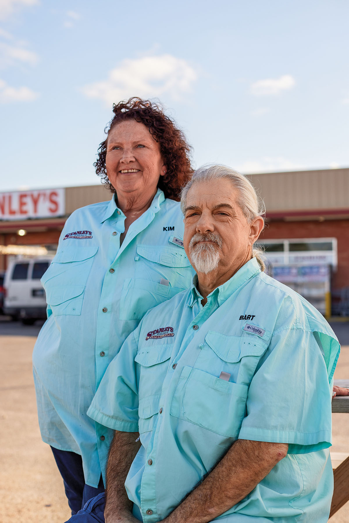Two people in pale blue shirts stand in front of a store with a sign reading "Stanley's"